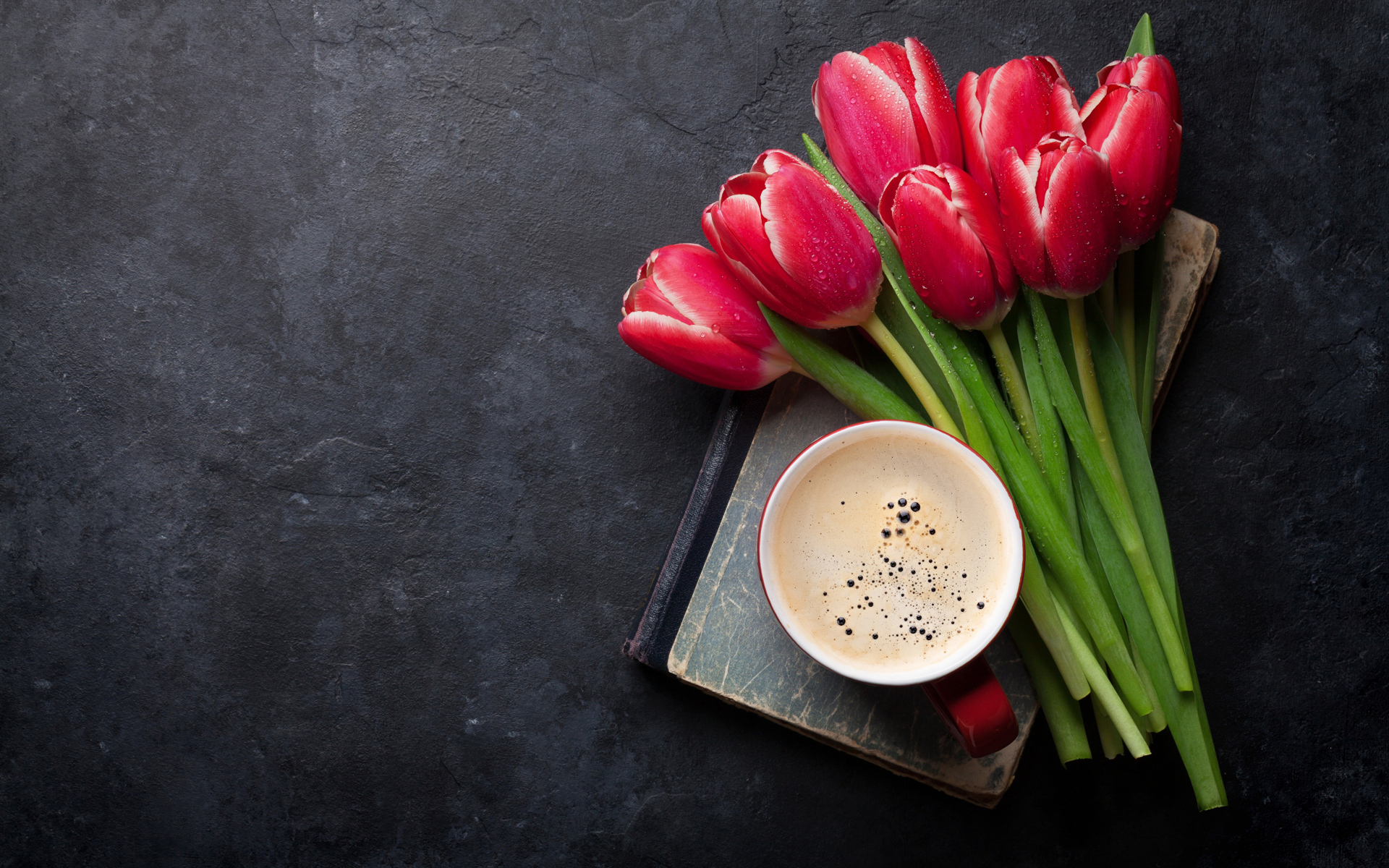 Букет красных тюльпанов с чашкой кофе на черном столе
