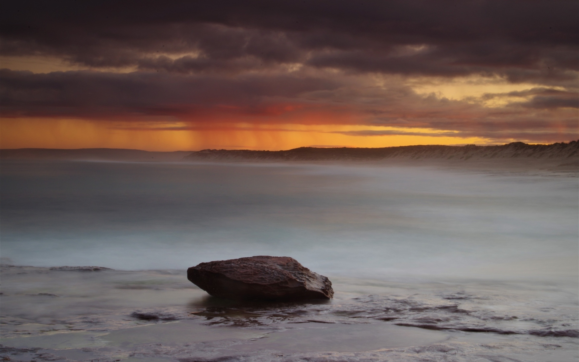 Большой камень в воде на фоне грозового неба в море