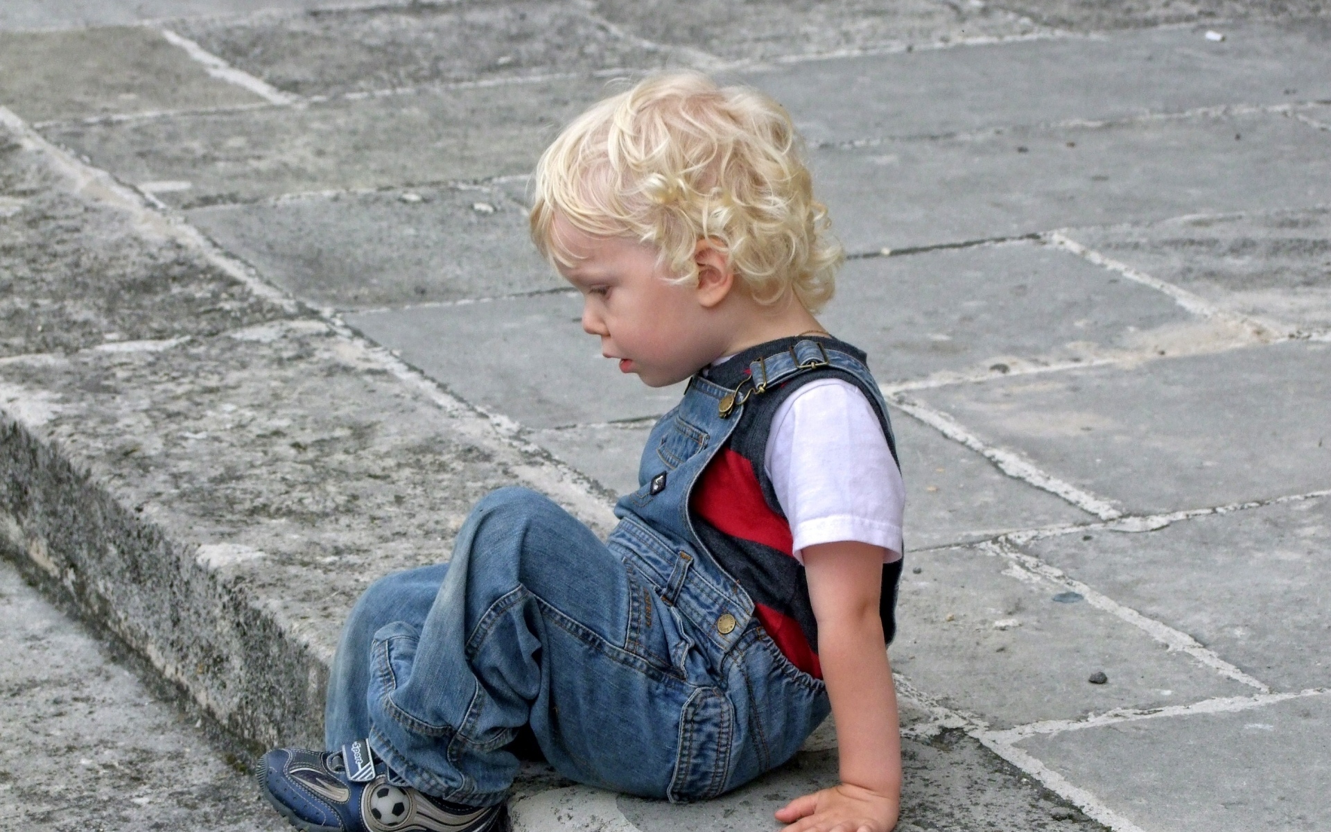 Мальчик в джинсовом комбинезоне сидит на дороге