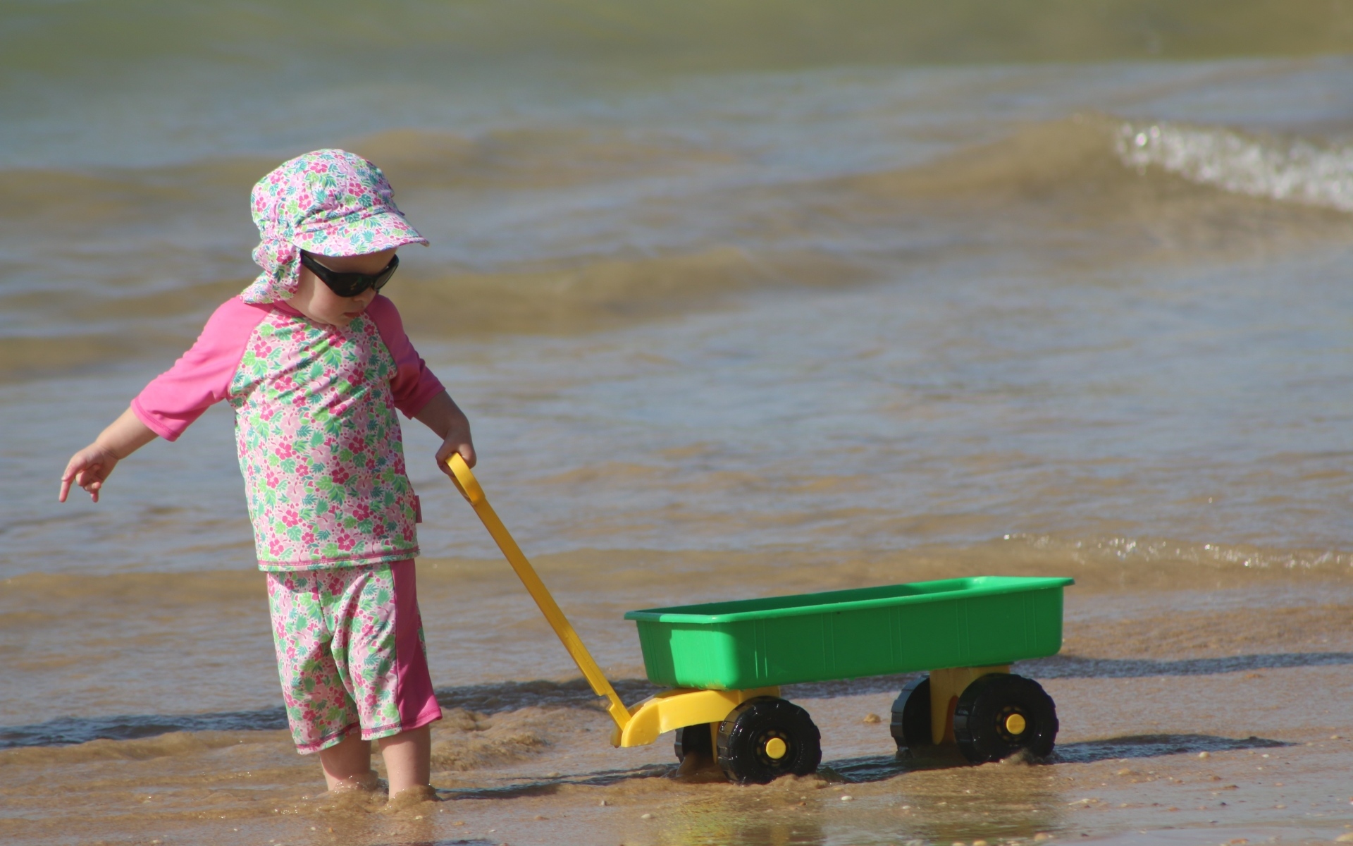 Девочка с машинкой играет на песке у моря
