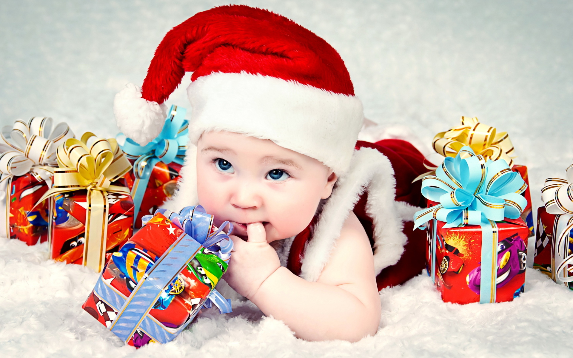 Грудной ребенок в новогодней шапке с подарками на покрывале