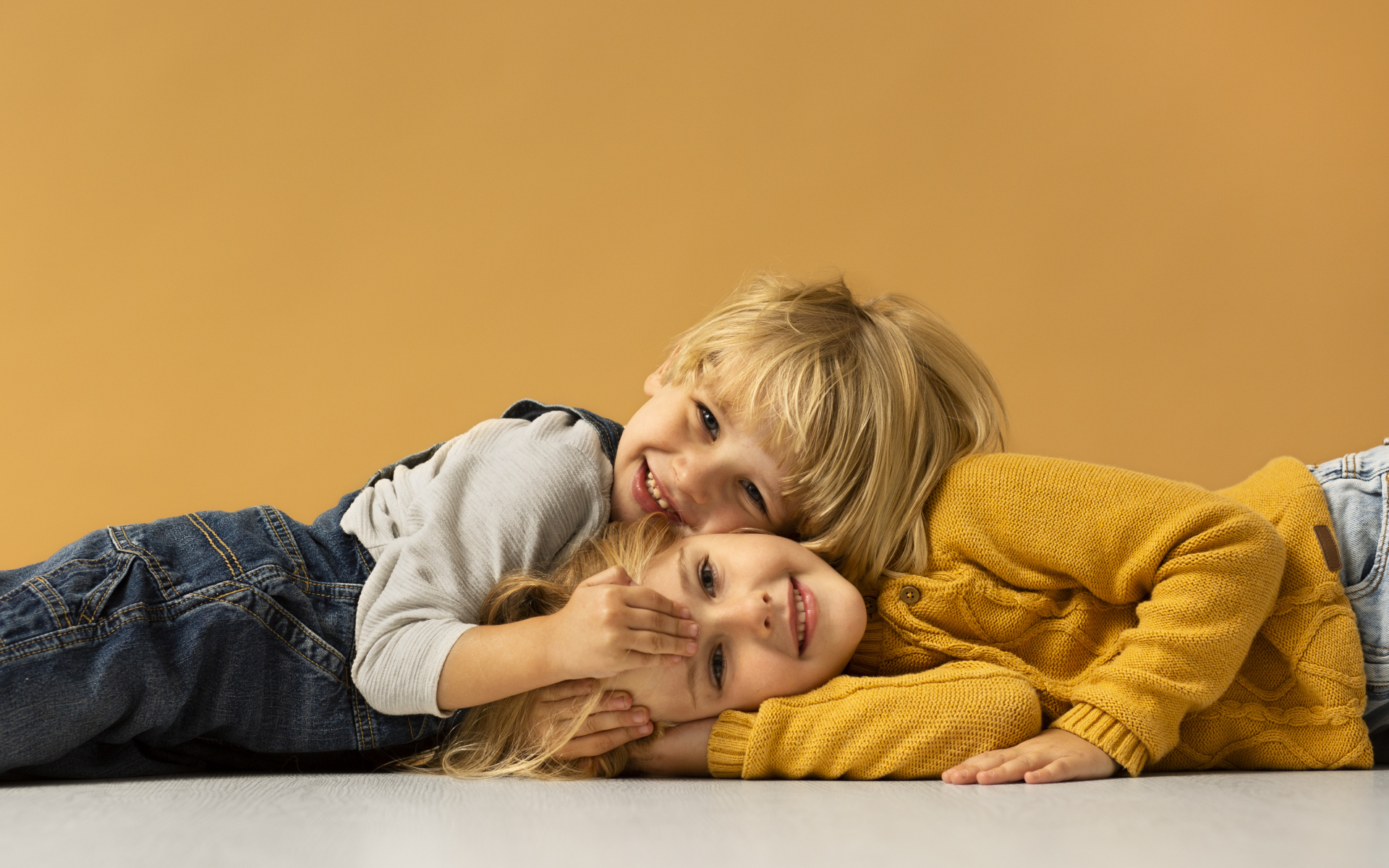Маленькие брат и сестра лежат на полу на желтом фоне