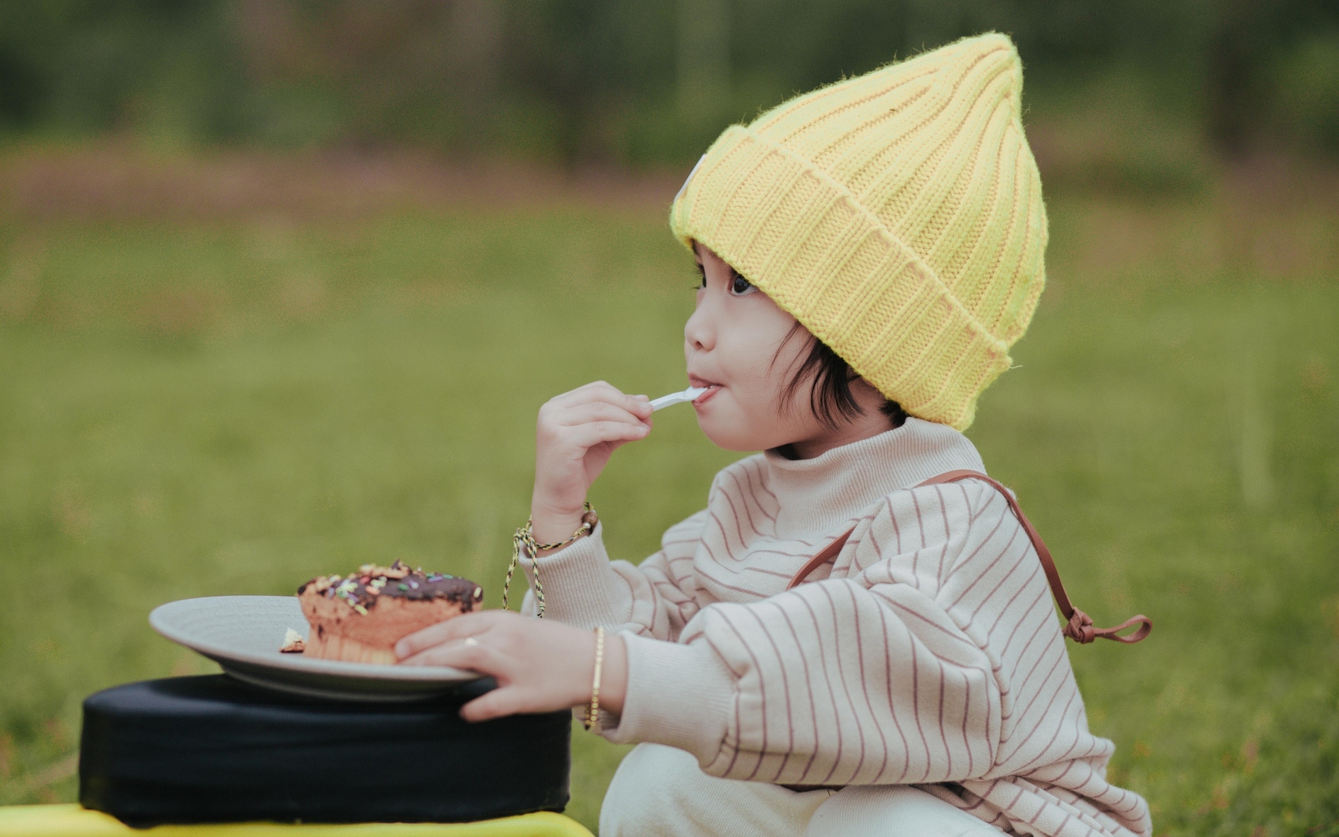 Маленькая девочка в желтой шапке ест пирожное