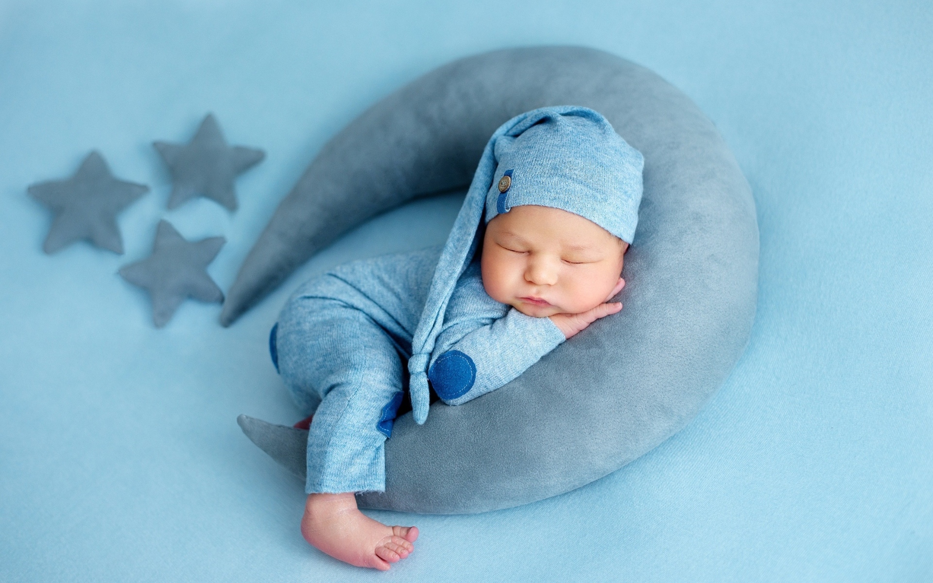 Новорожденный малыш спит на игрушечном полумесяце на голубом фоне