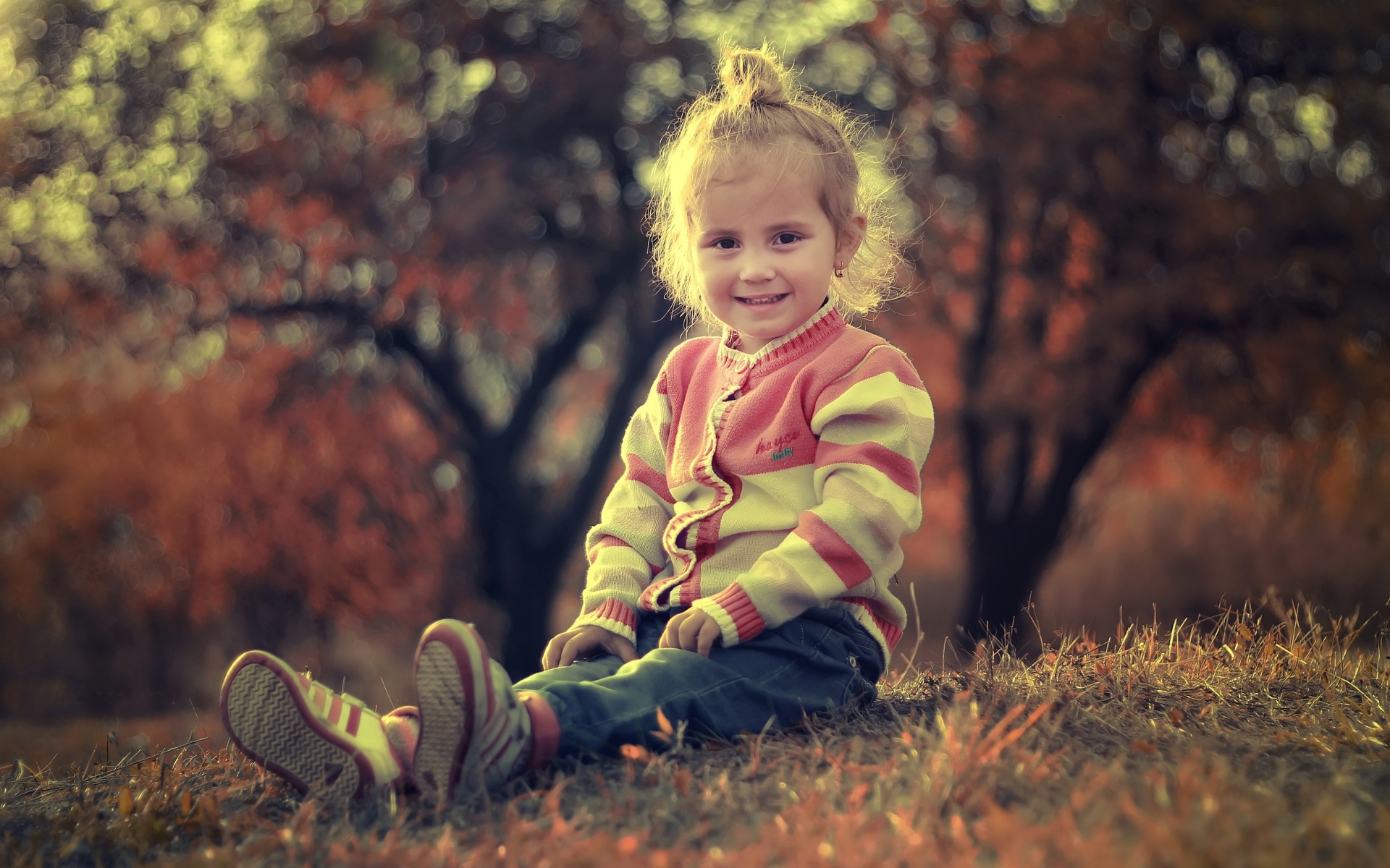 Настоящая маленькая девочка сидит на земле в лучах солнца