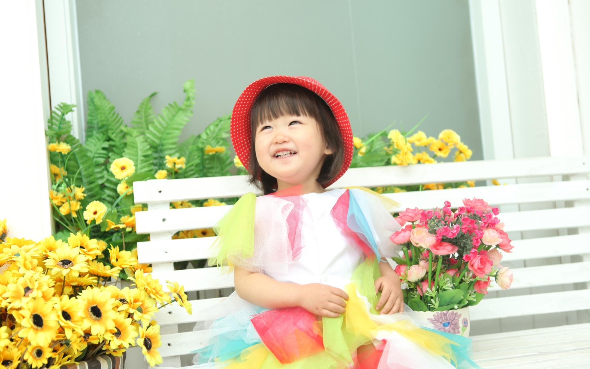 Улыбающаяся девочка азиатка сидит на лавке с цветами