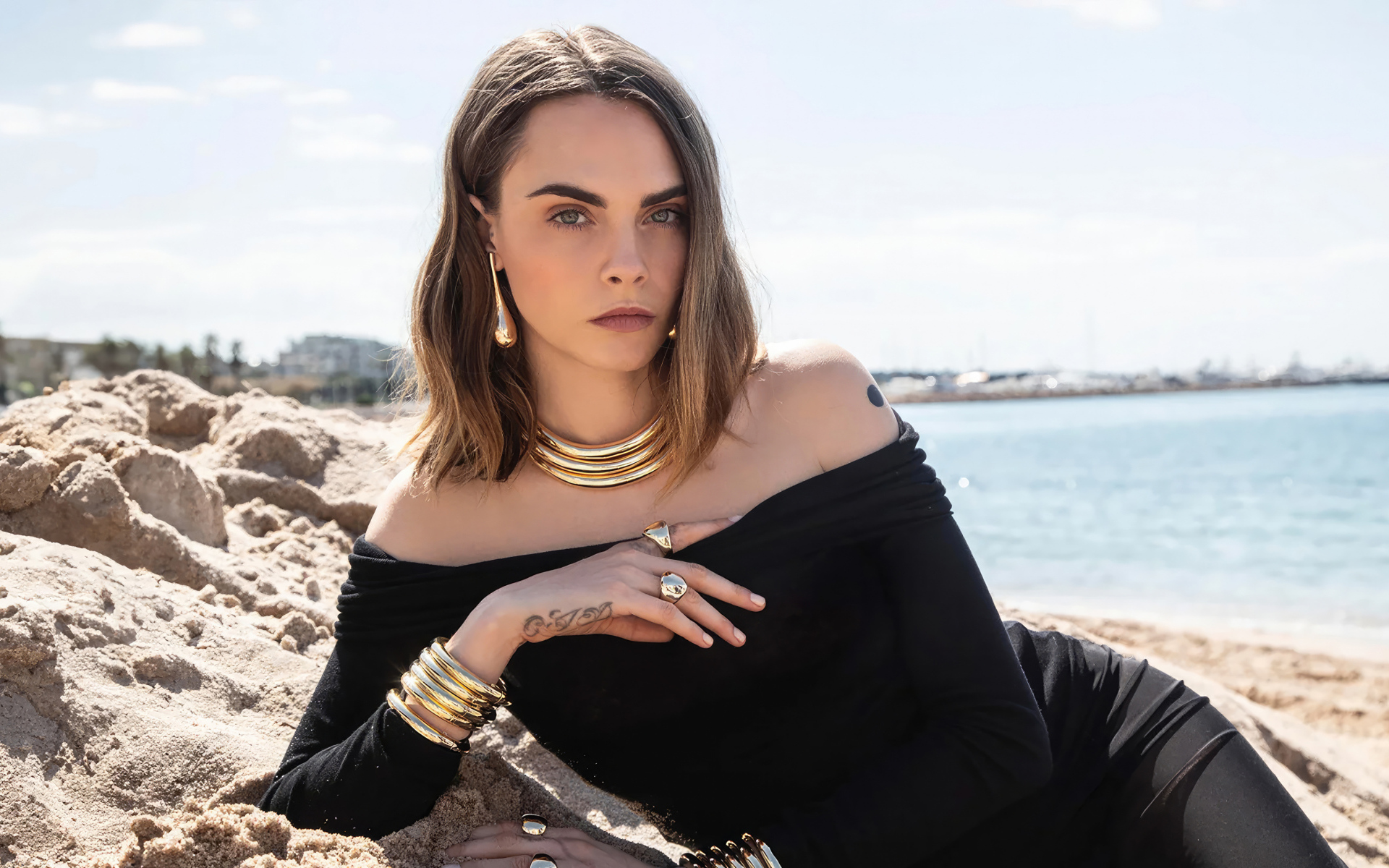 Кара Делевинь в черном платье лежит на песке