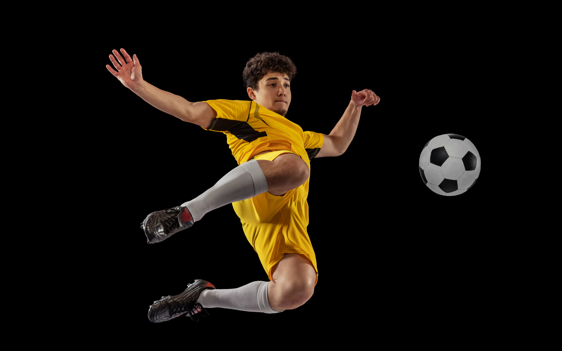Мужчина футболист отбивает мяч на черном фоне
