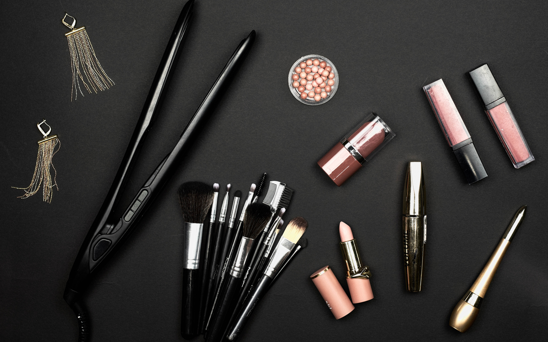 Кисточки с косметикой и плойкой на черном фоне