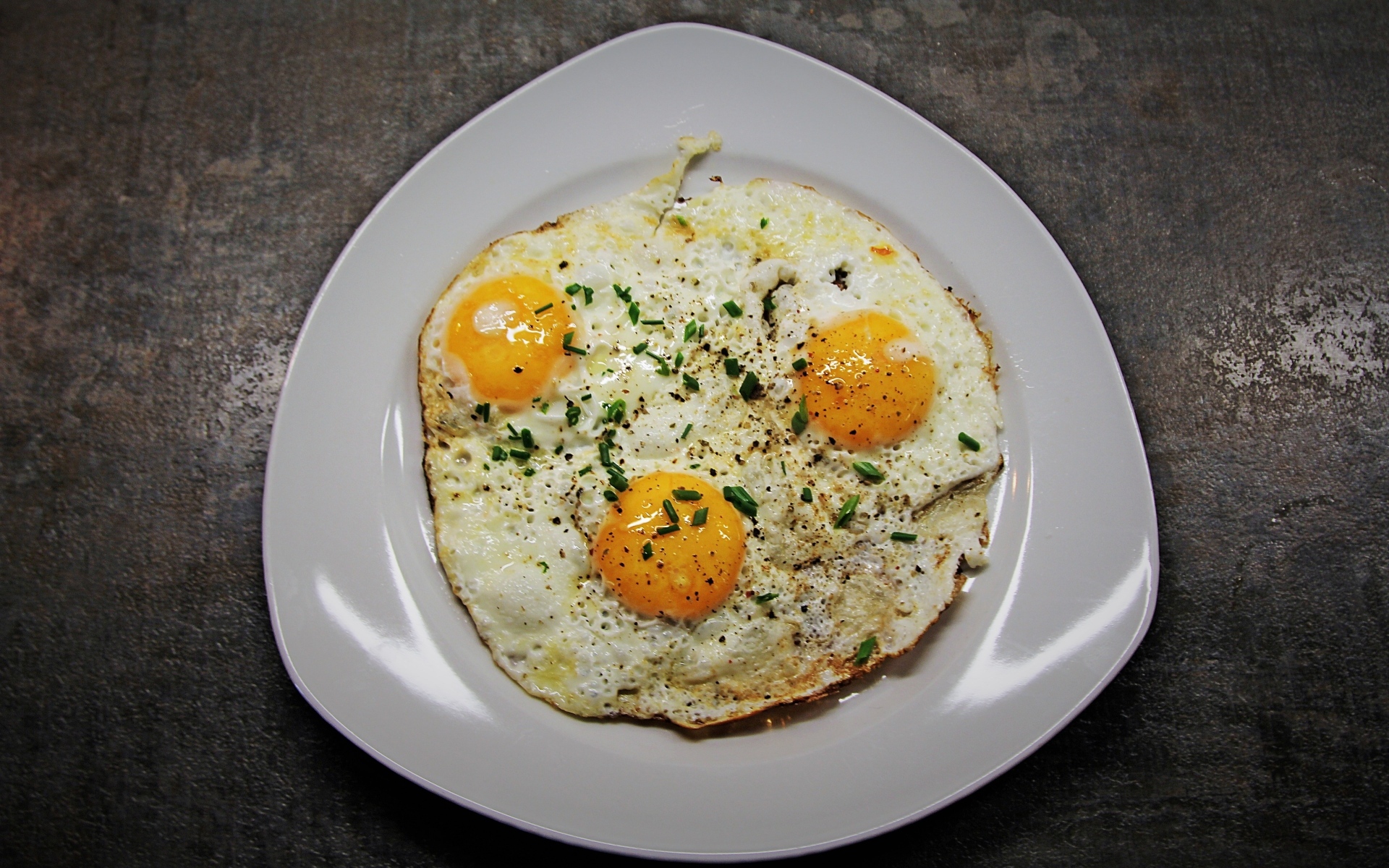 Яичница глазунья в тарелке на сером столе