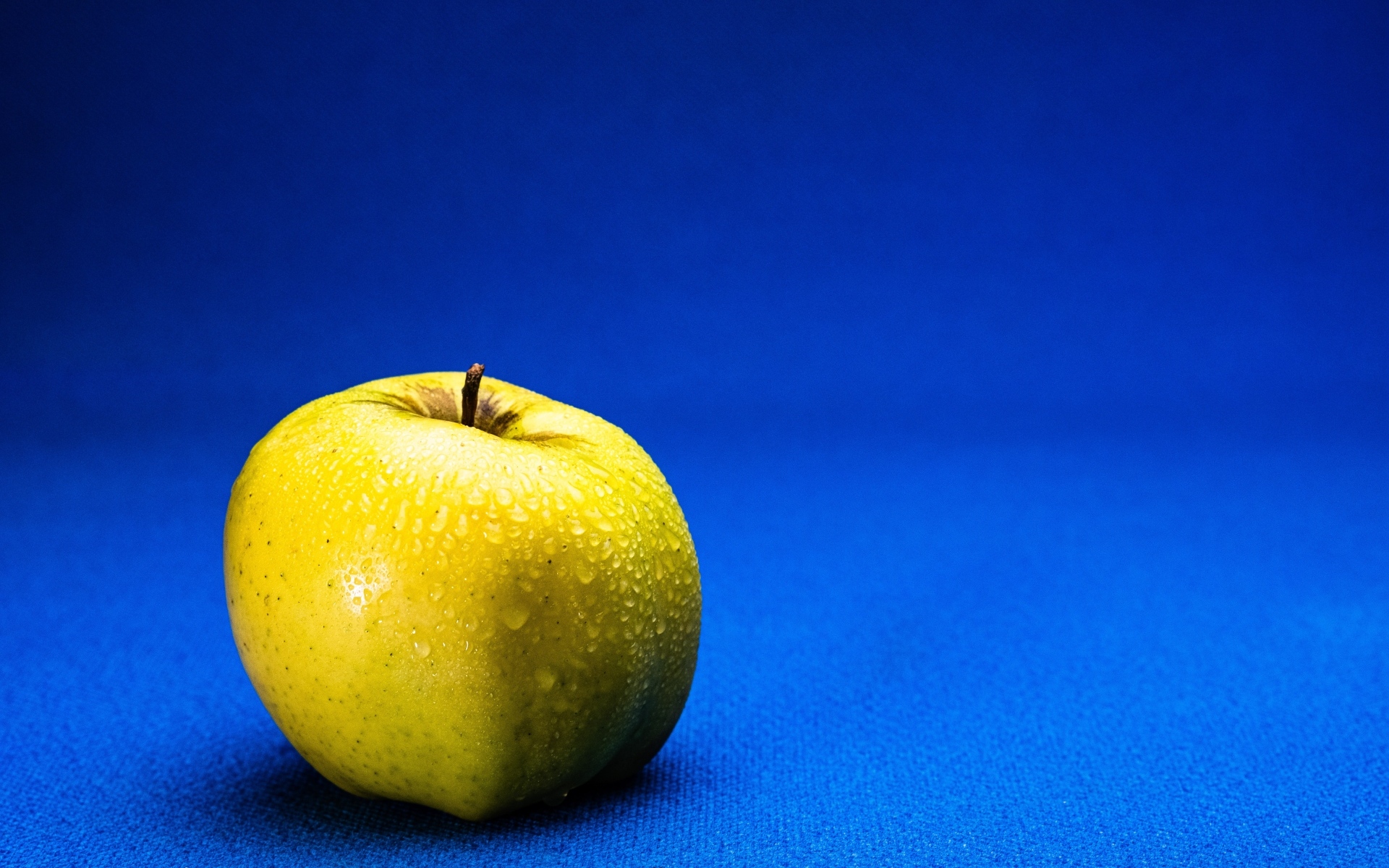 Большое желтое мокрое яблоко на синем фоне