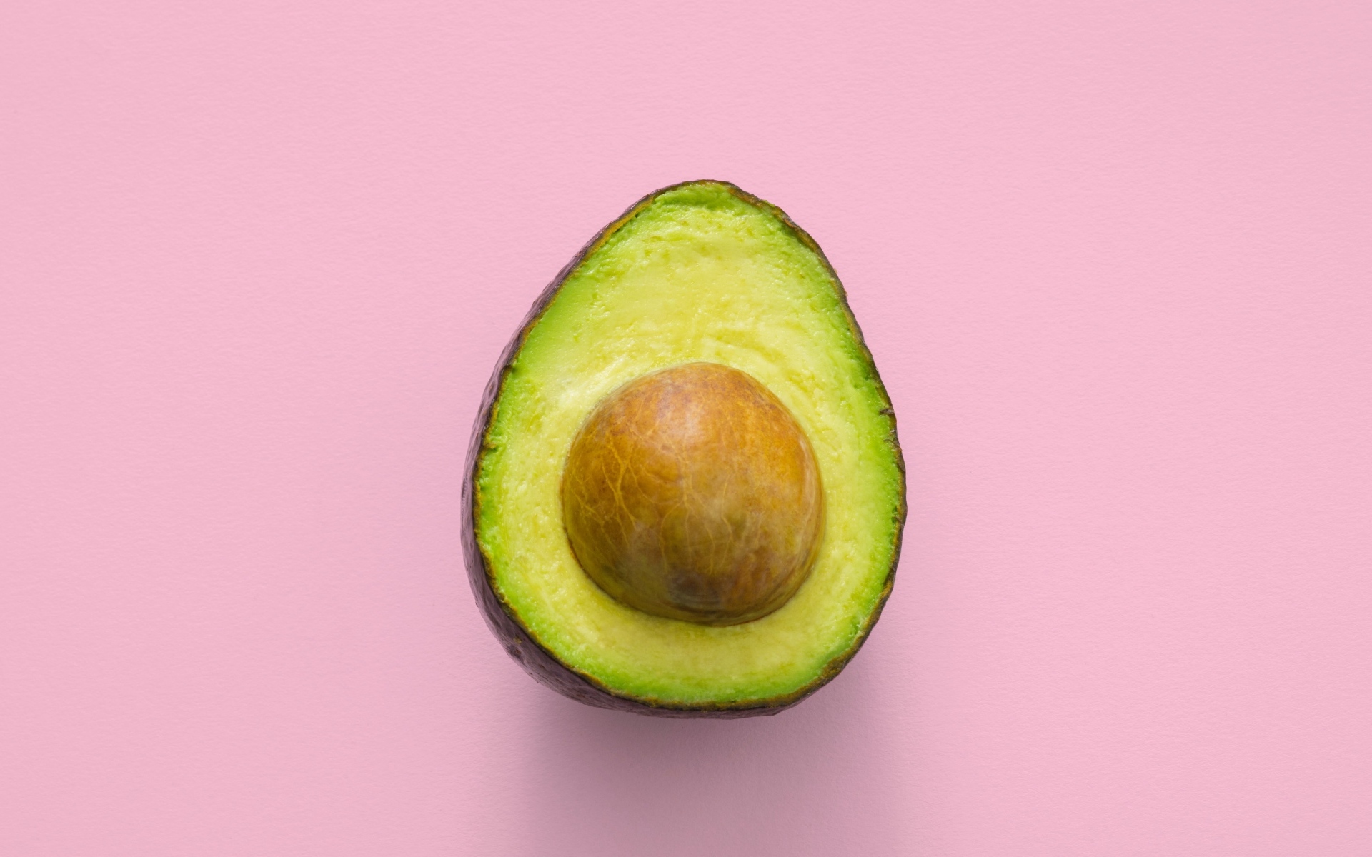 Половина авокадо с большой косточкой на розовом фоне
