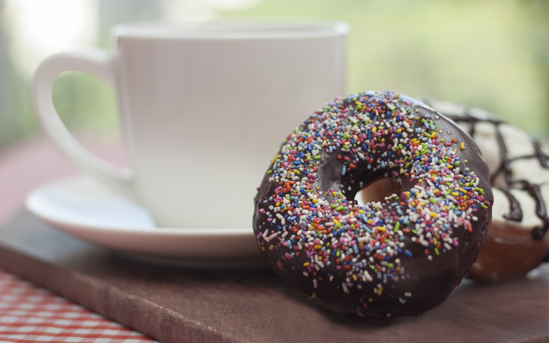 Донат с шоколадной глазурью и сладкой посыпкой на столе с чашкой чая