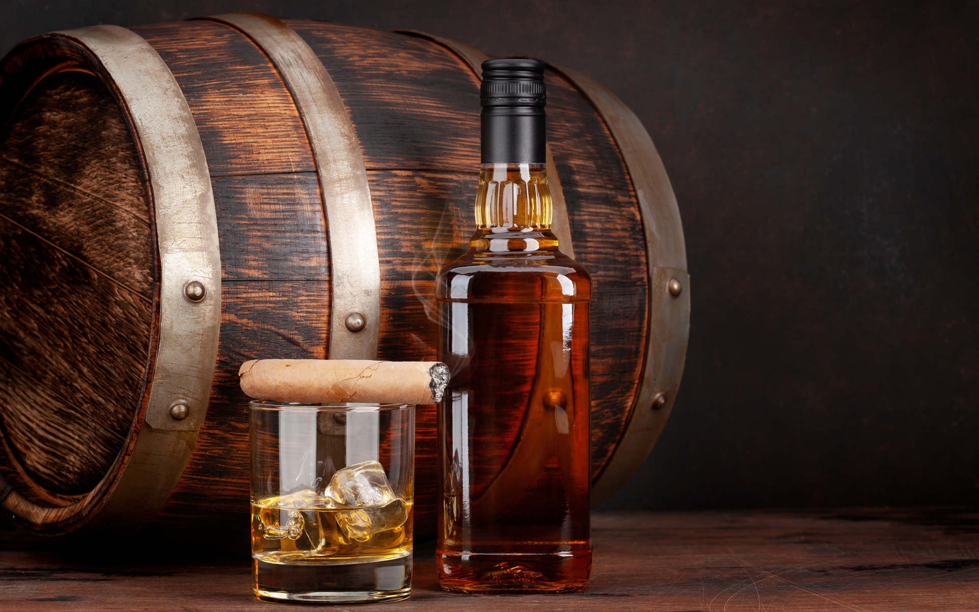 Бутылка виски на столе со стаканом, сигарой и бочкой