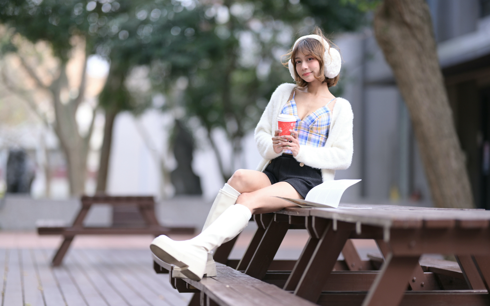 Девушка азиатка с кофе сидит на столе в парке