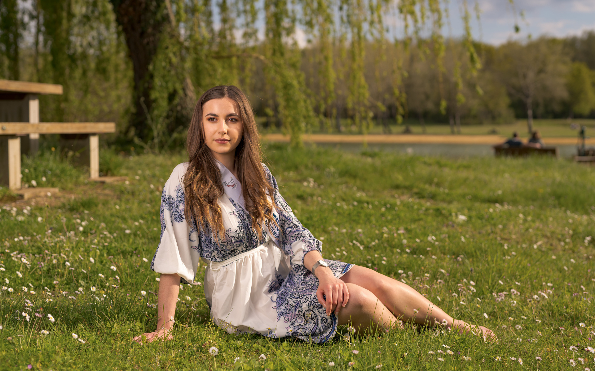 Красивая девушка в платье сидит на зеленой траве в парке