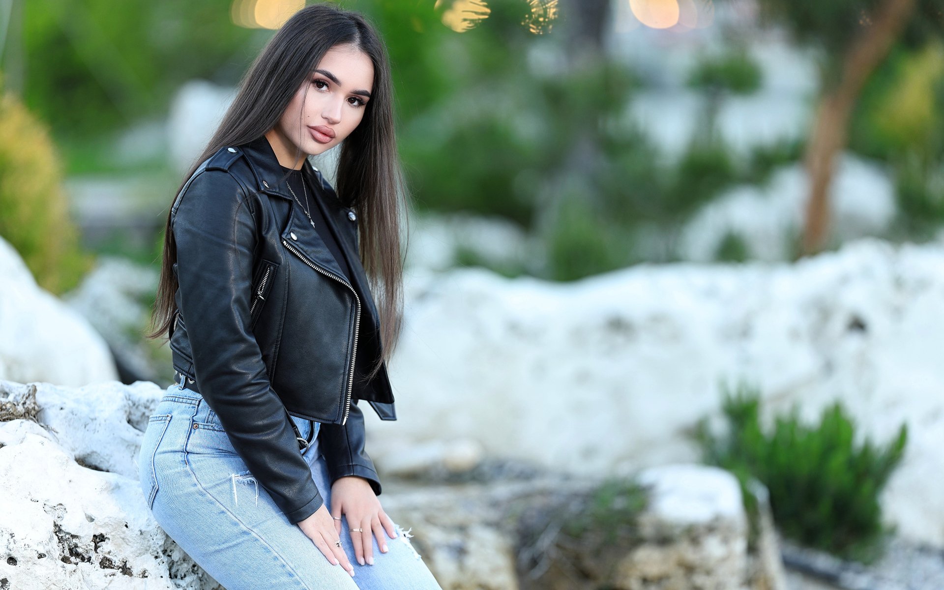 Брюнетка в черной кожаной куртке сидит на камне