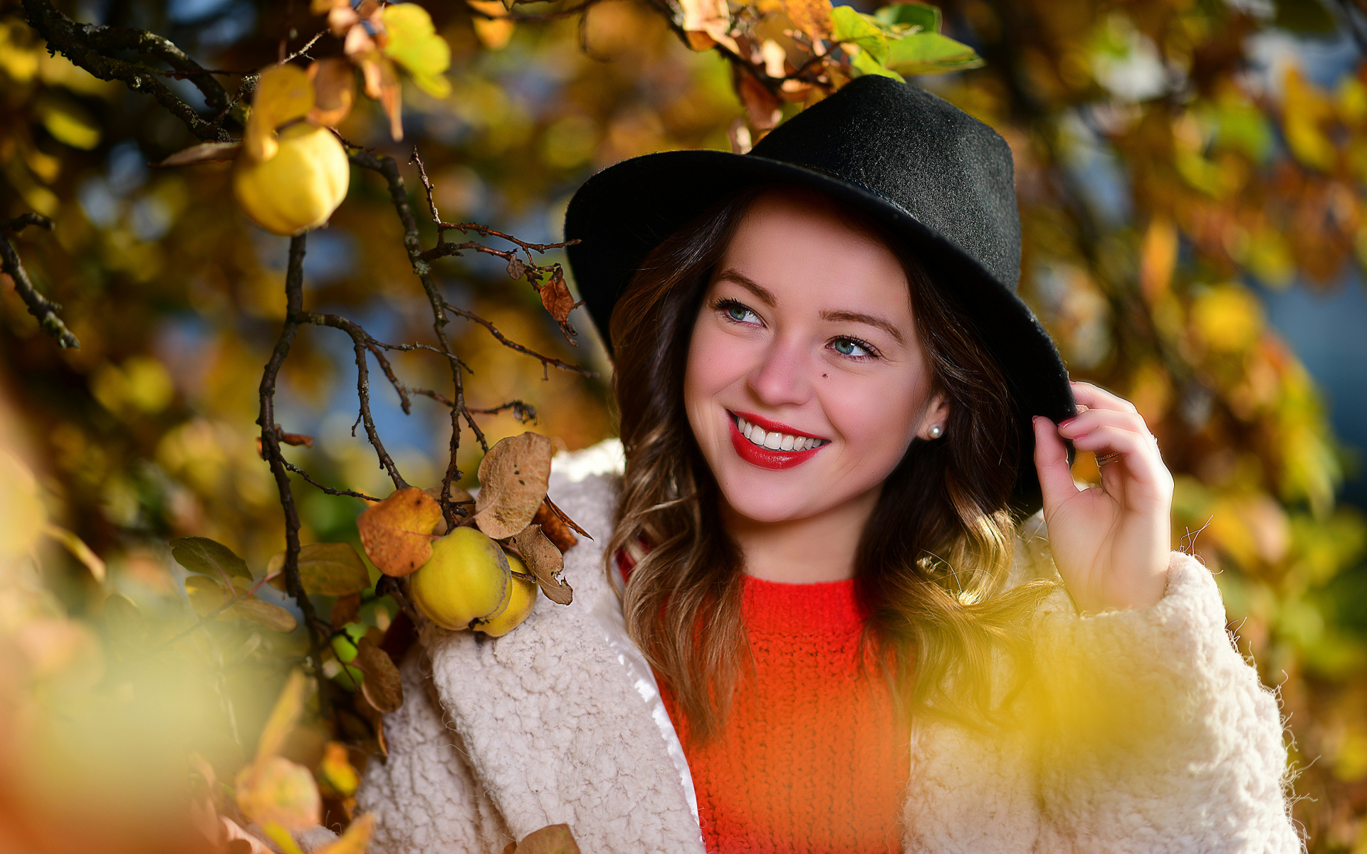 Улыбающаяся девушка в черной шляпе у дерева с яблоками