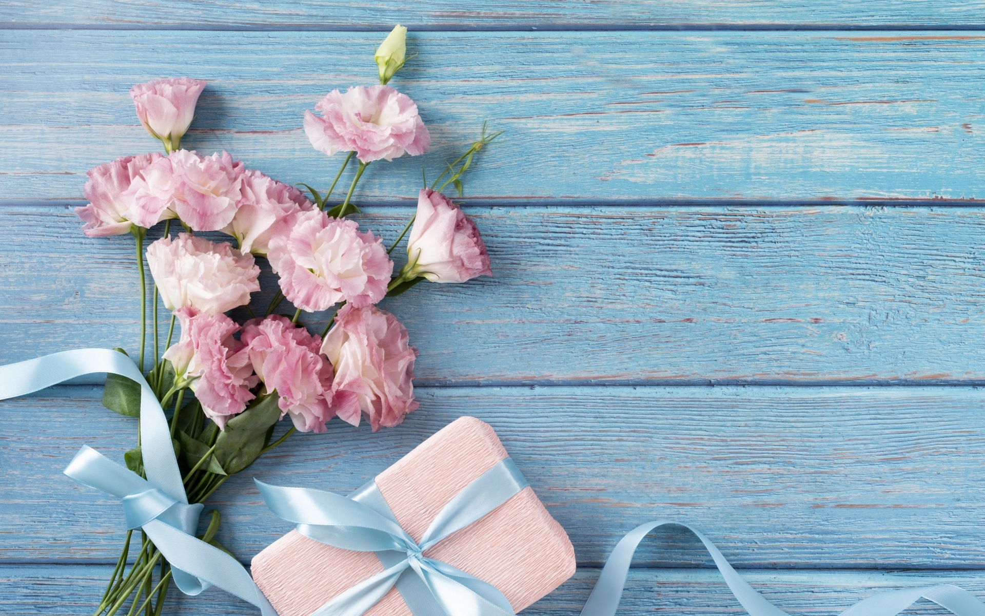 Букет розовых цветов эустомы с подарком на голубом столе