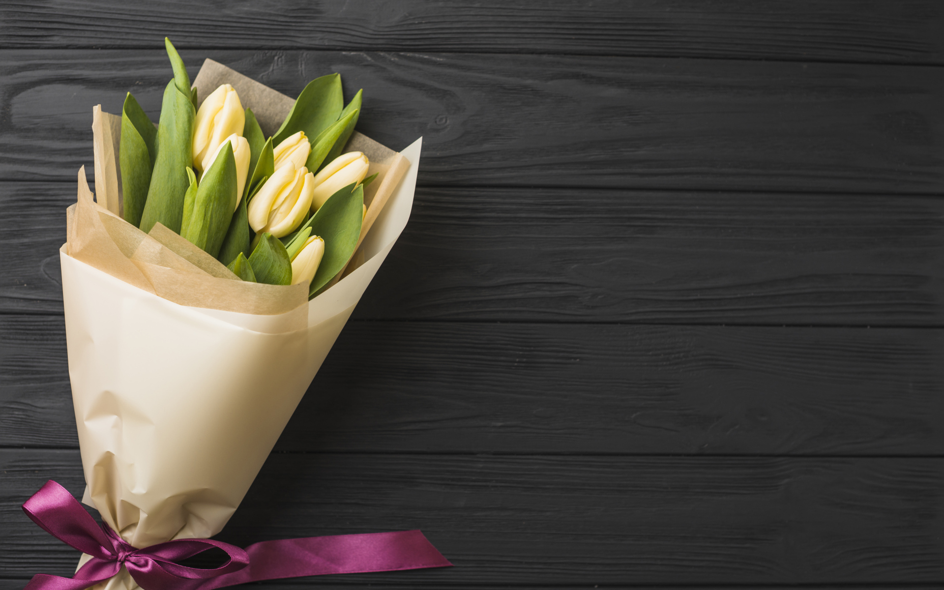 Букет желтых тюльпанов в бумаге на черном столе