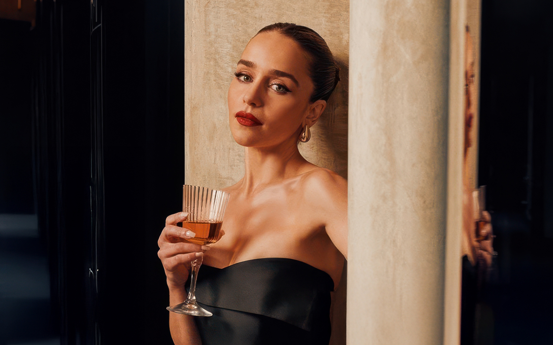 Актриса Эмилия Кларк с бокалом стоит у стены