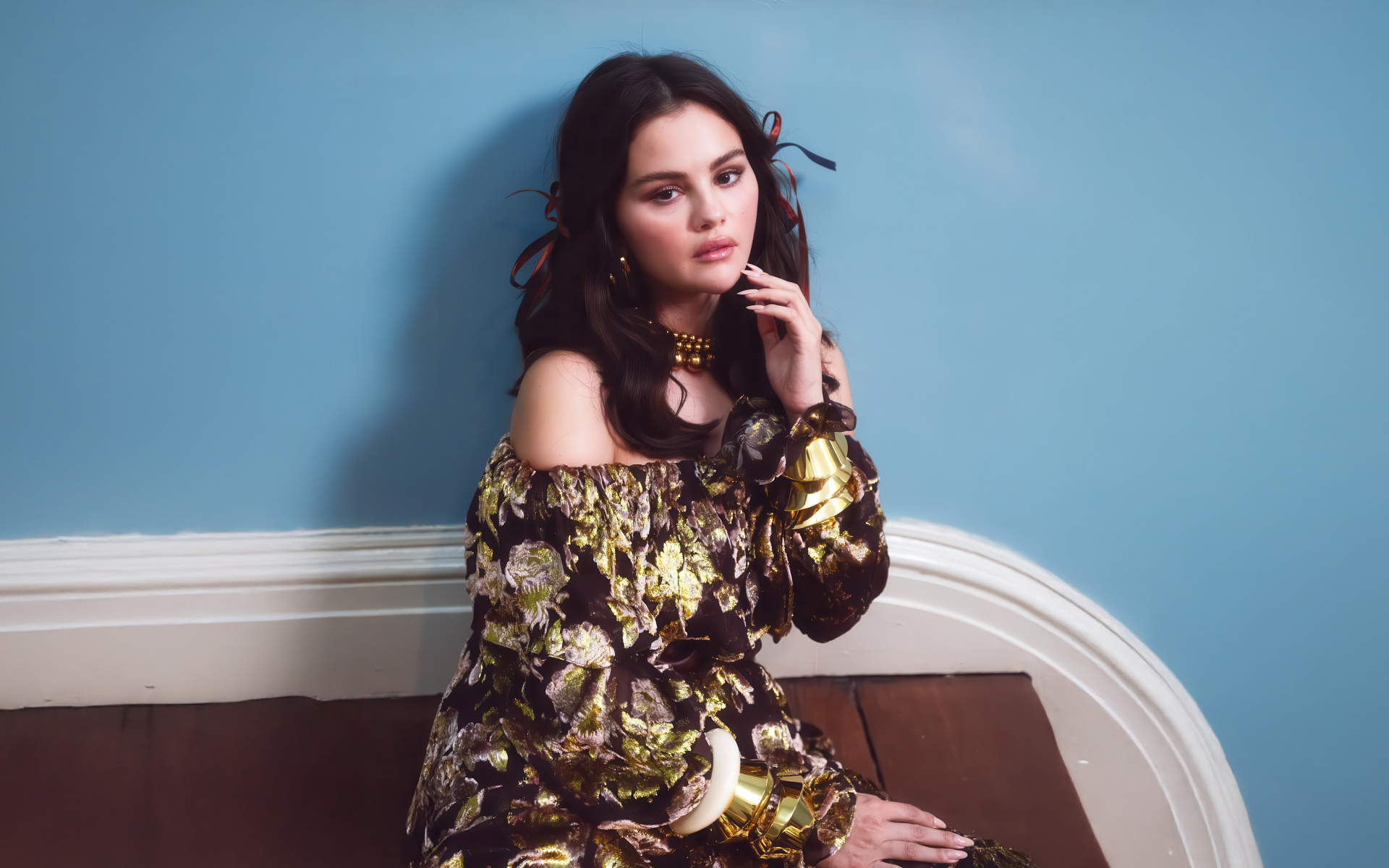 Актриса Селена Гомес на диване на фоне серой стены