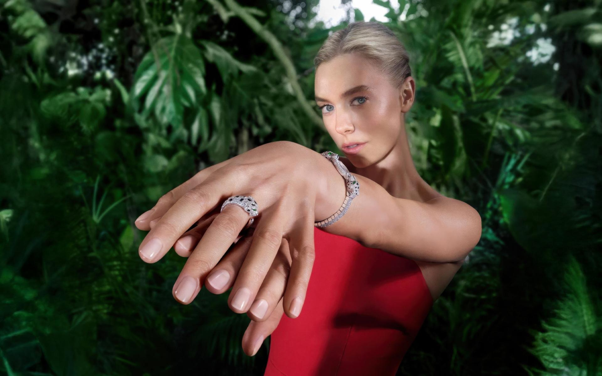 Актриса Ванесса Кирби в красном платье с кольцом на руке на фоне зарослей