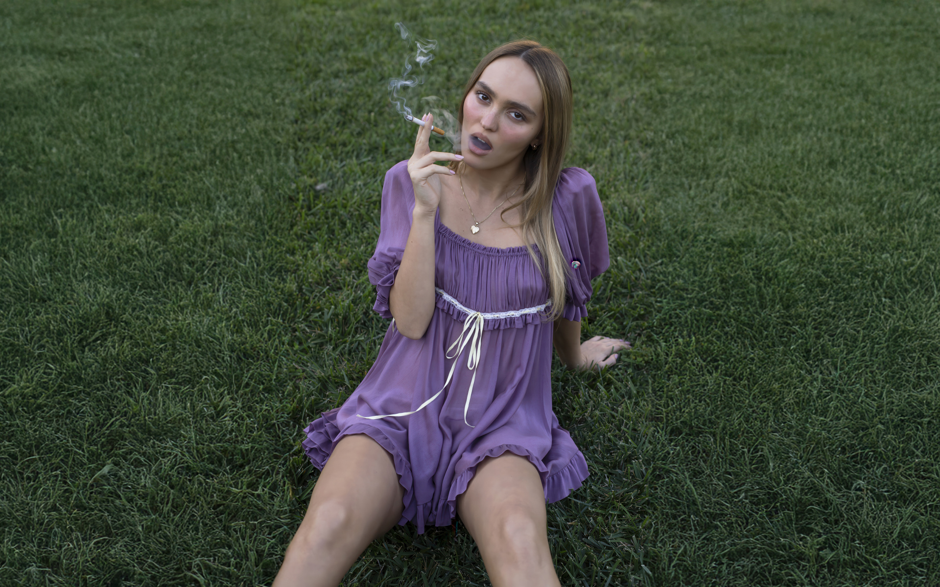 Молодая Лили-Роуз Депп с сигаретой сидит на траве