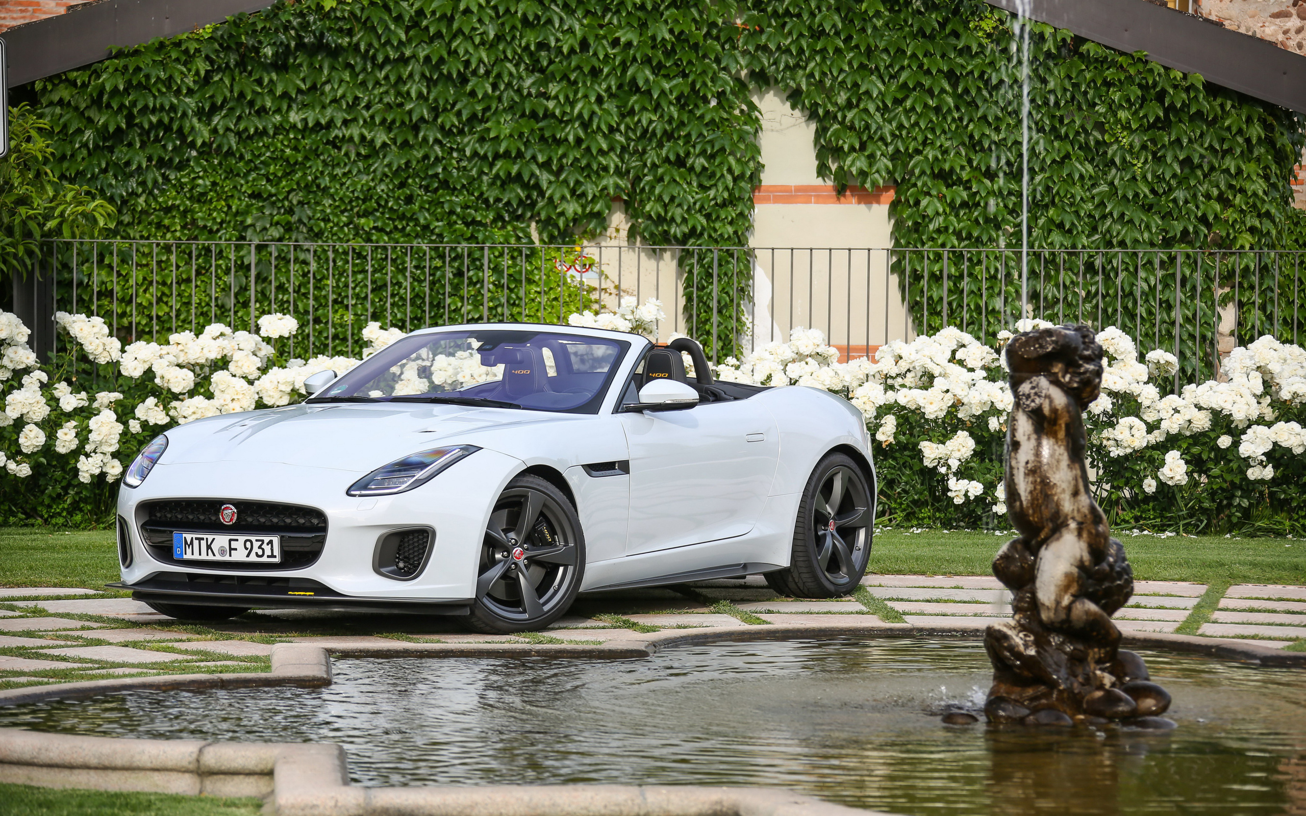Белый автомобиль кабриолет Jaguar F-Type у фонтана