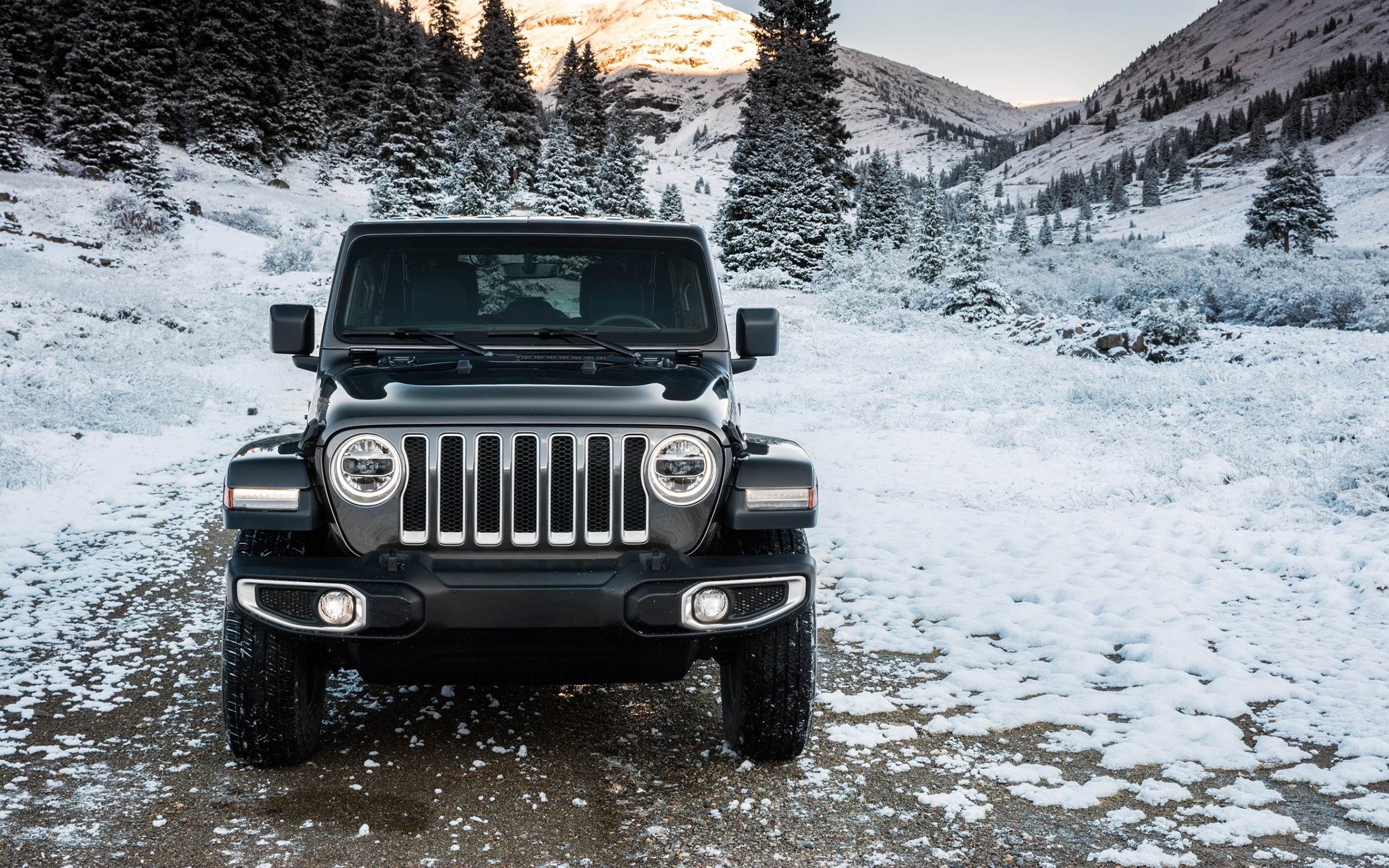 Внедорожник Jeep Wrangler Unlimited Sahara, 2018 на заснеженной дороге на фоне гор