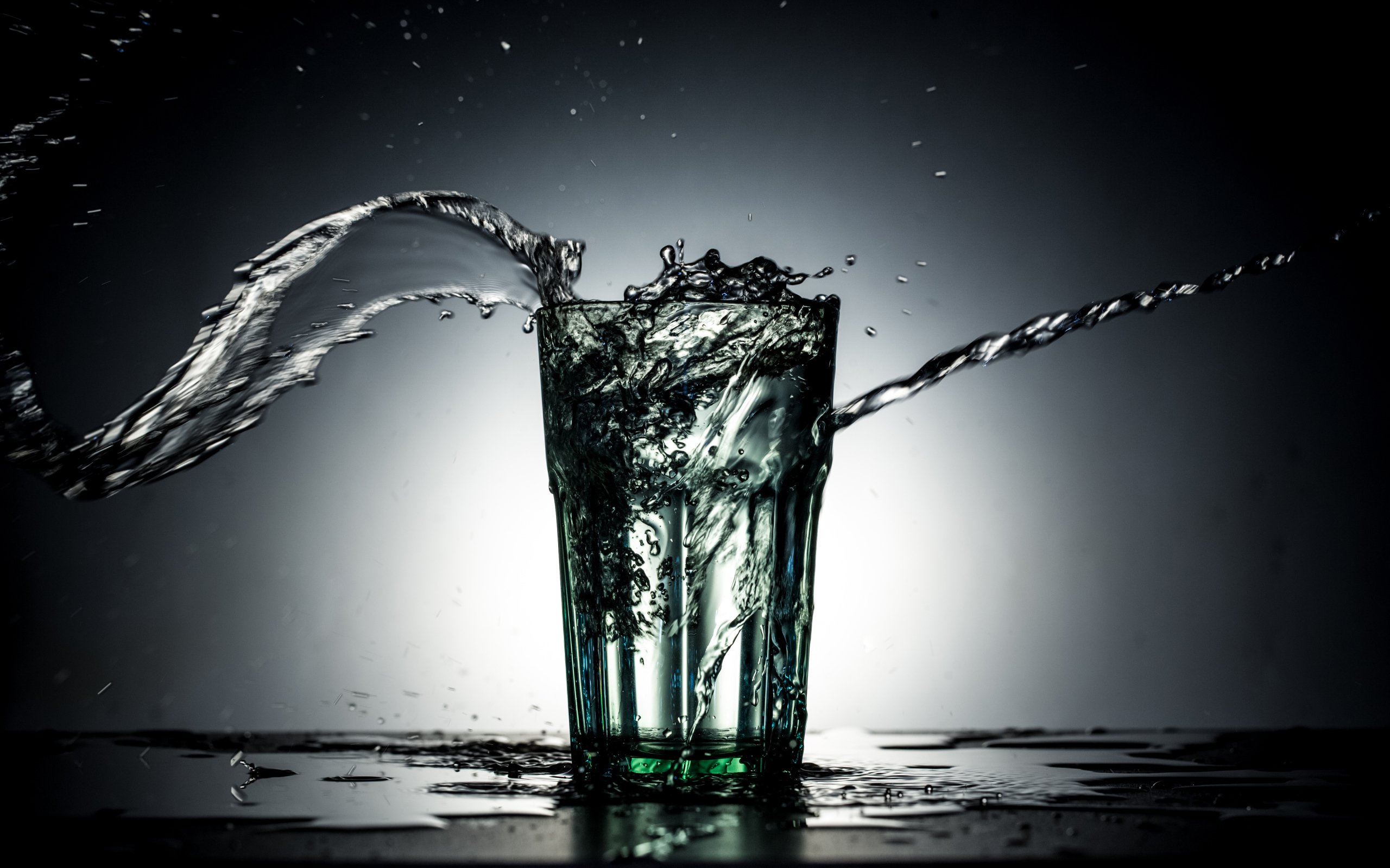 Брызги воды из стакана с водой на сером фоне