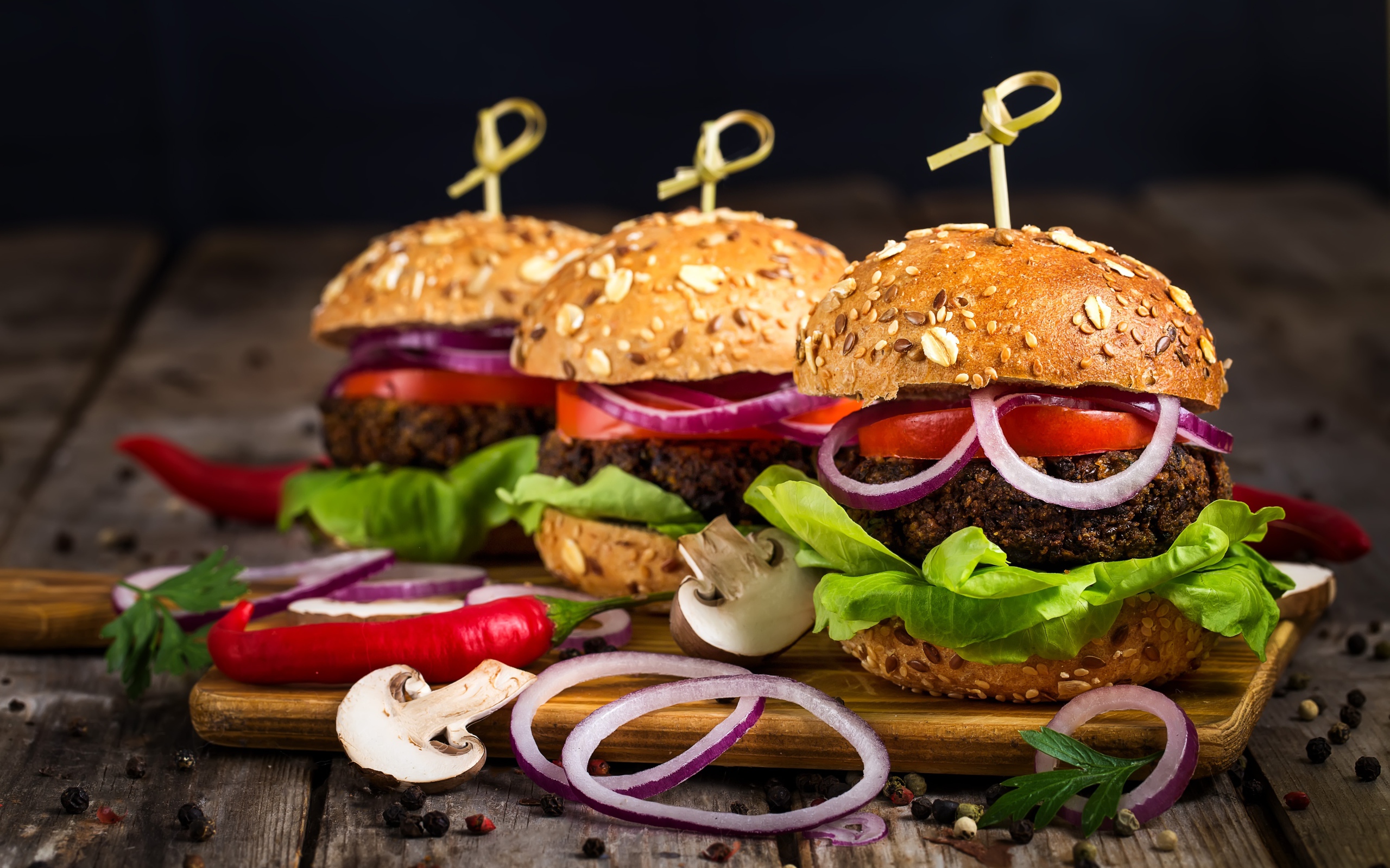 Три аппетитных гамбургера с кольцами лука и перцем