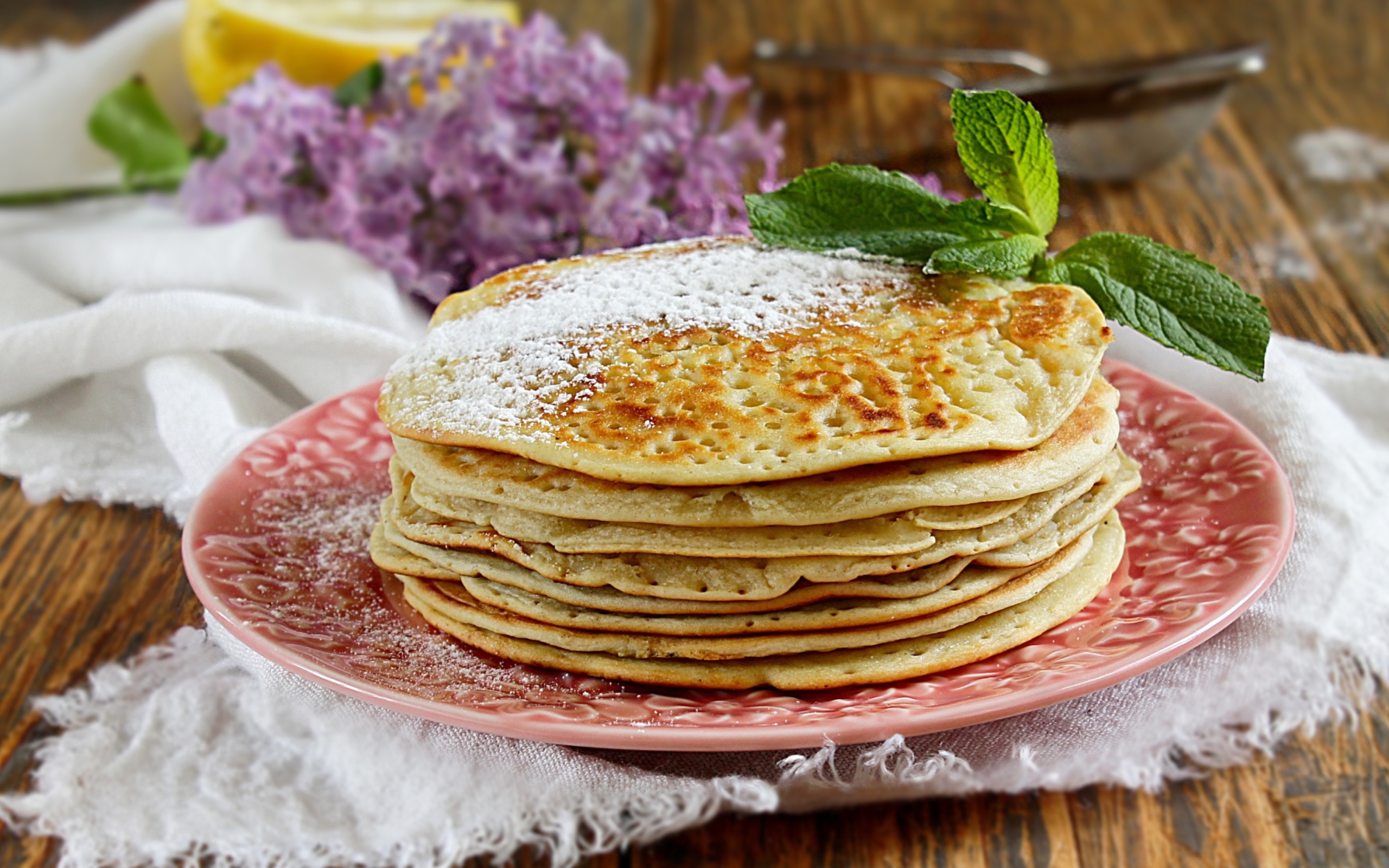 Тонкие блинчики на тарелке с сахарной пудрой и веточкой мяты