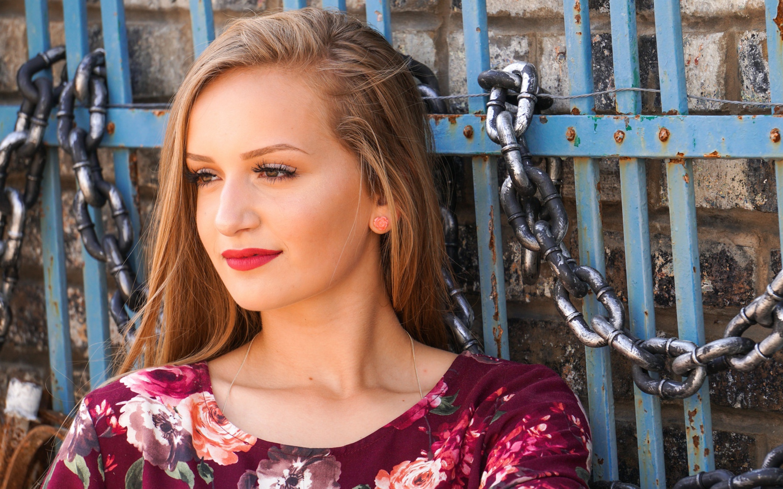 Красивая молодая девушка сидит у забора с железными цепями