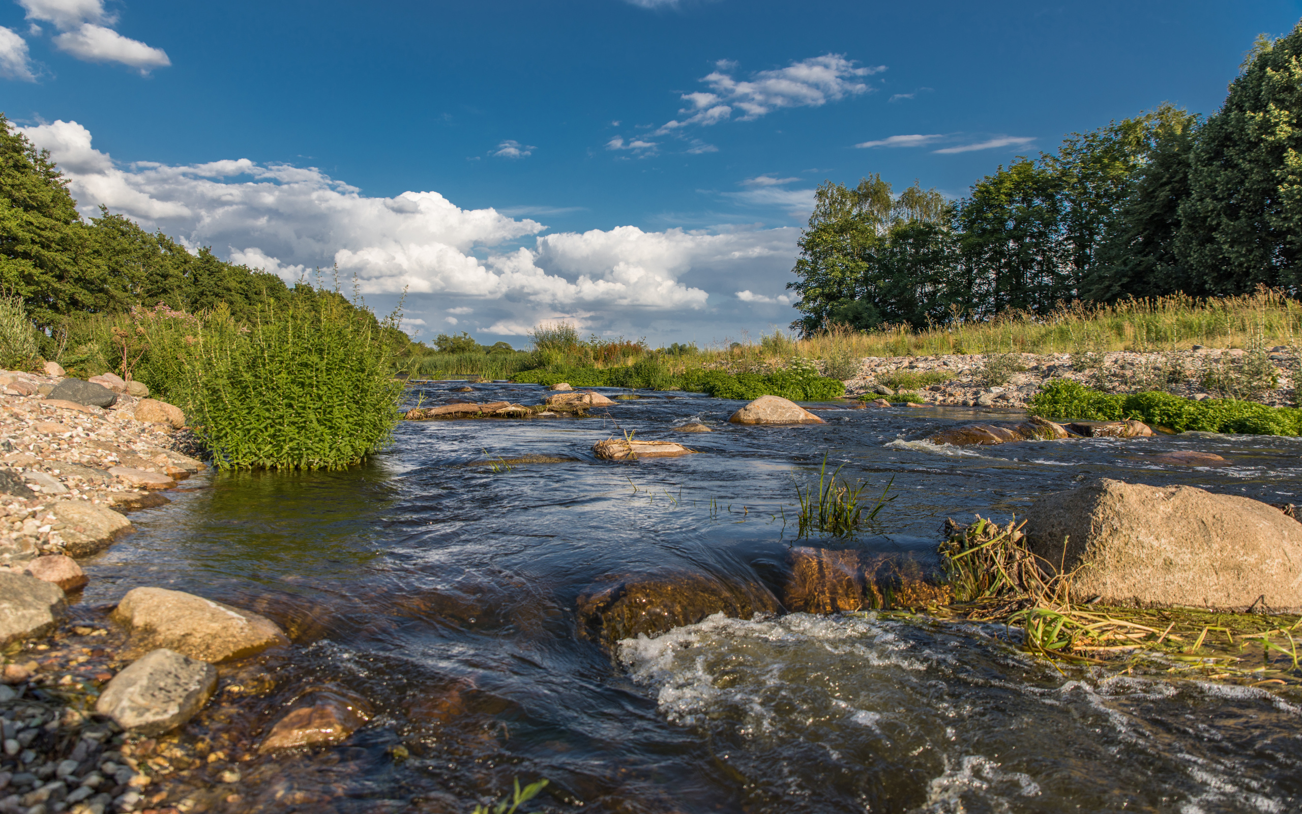 Быстрая речная вода стекает по камням под красивым голубым небом