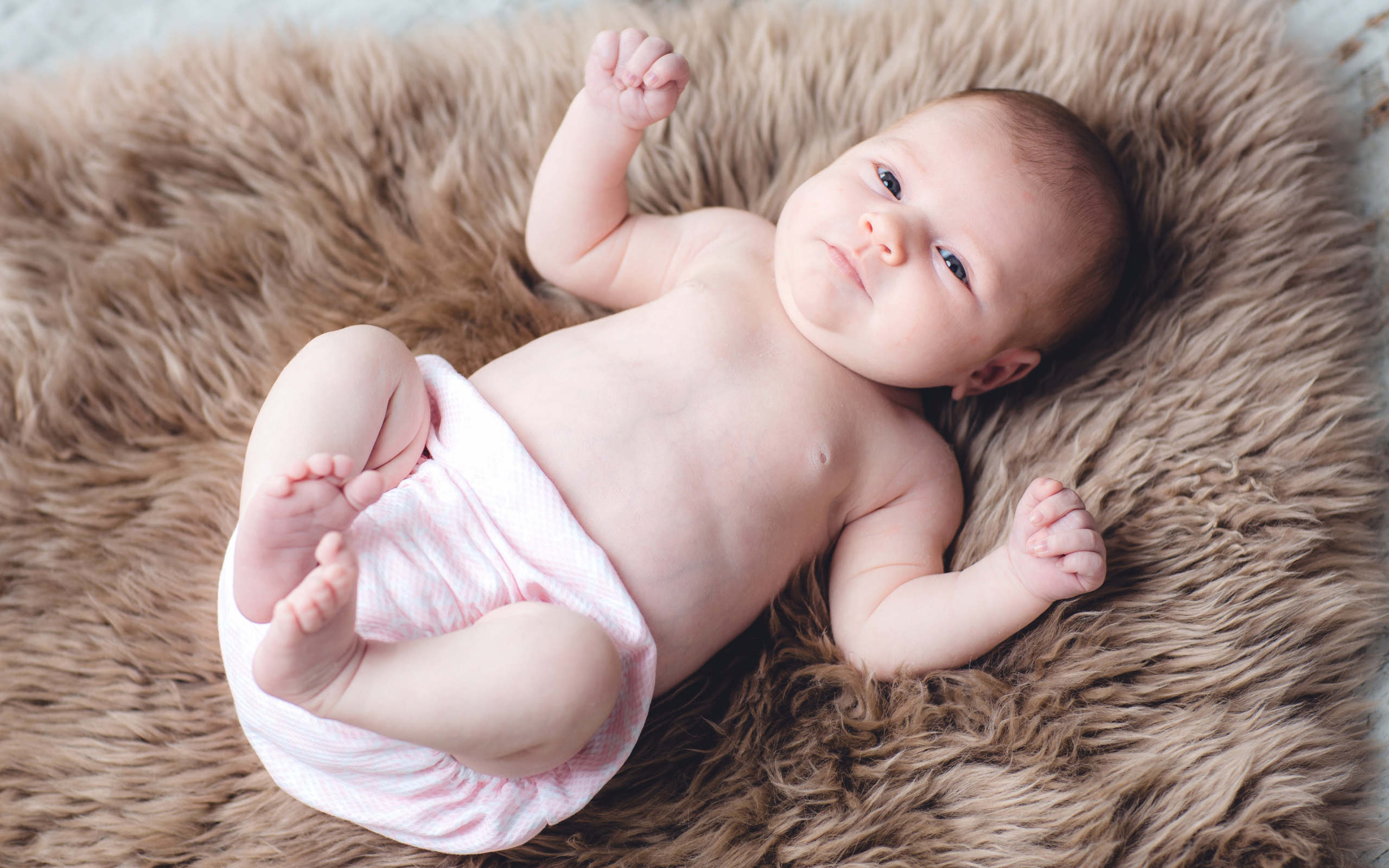 Грудной ребенок лежит на меховом покрывале