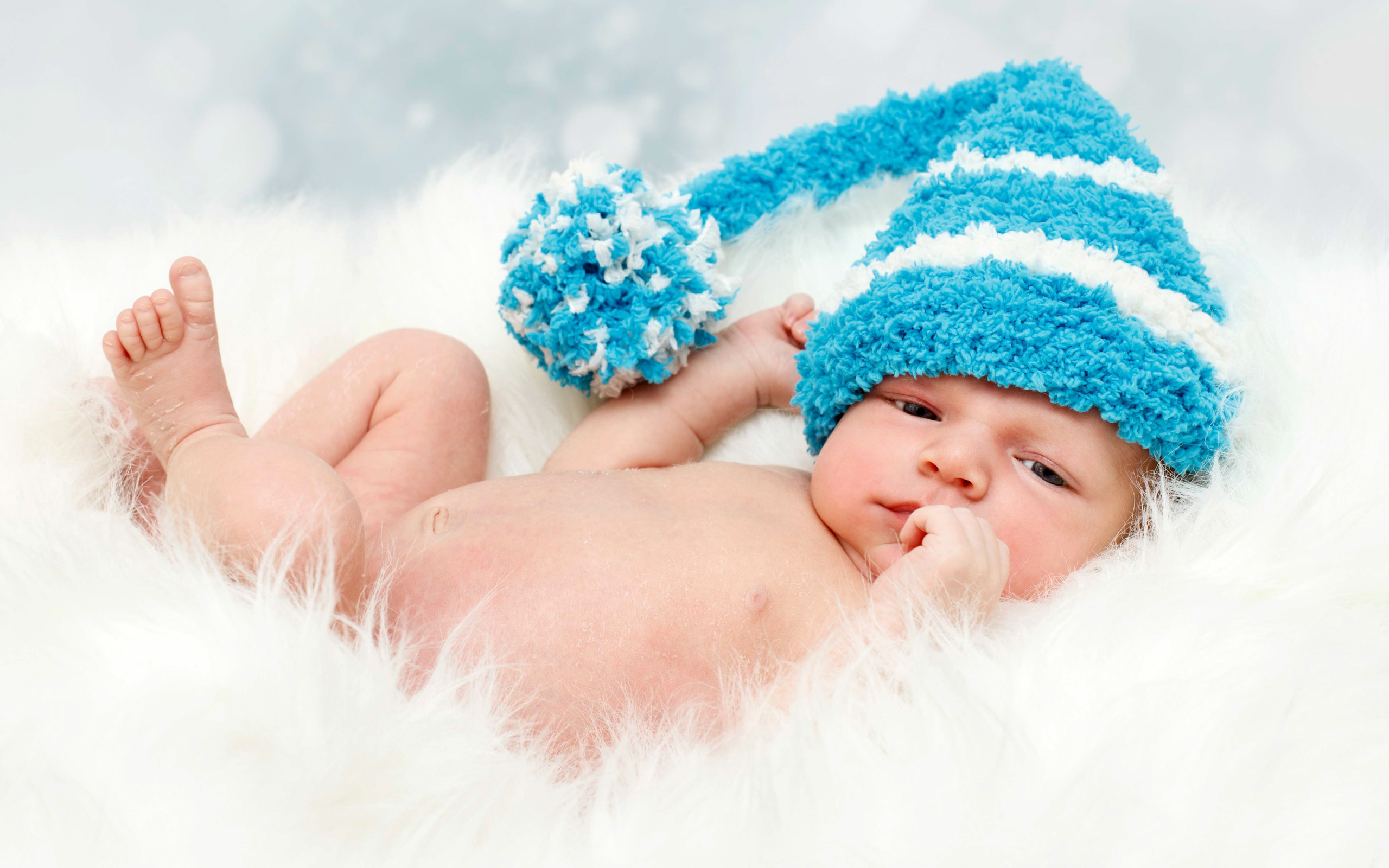 Грудной ребенок в голубой шапке с бубоном на голове