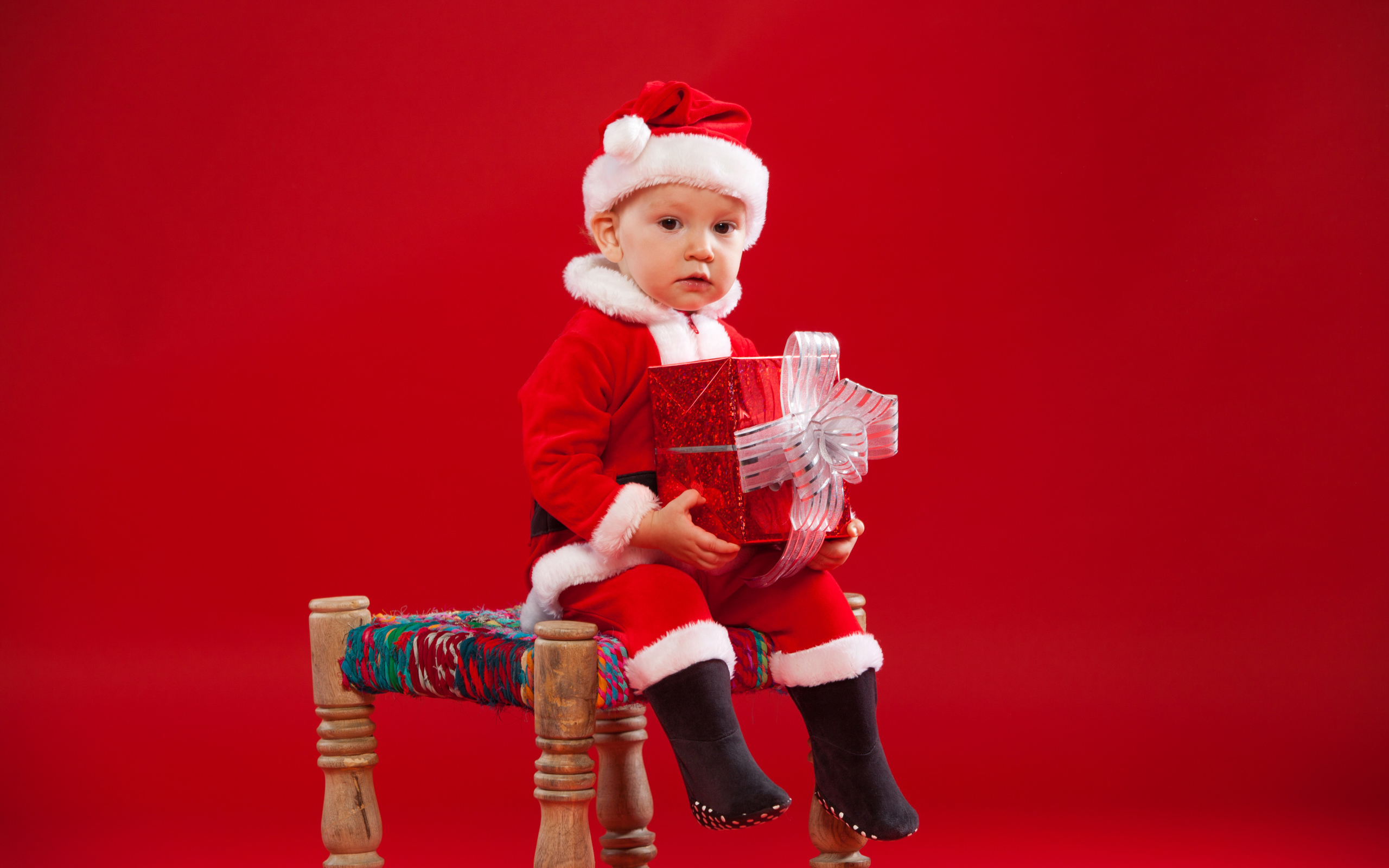 Маленький мальчик сидит на стуле с новогодним подарком