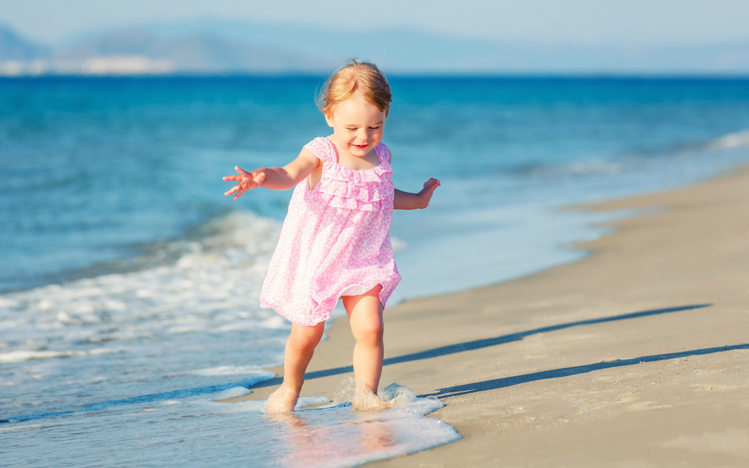 Маленькая девочка в розовом платье гуляет по морскому песку