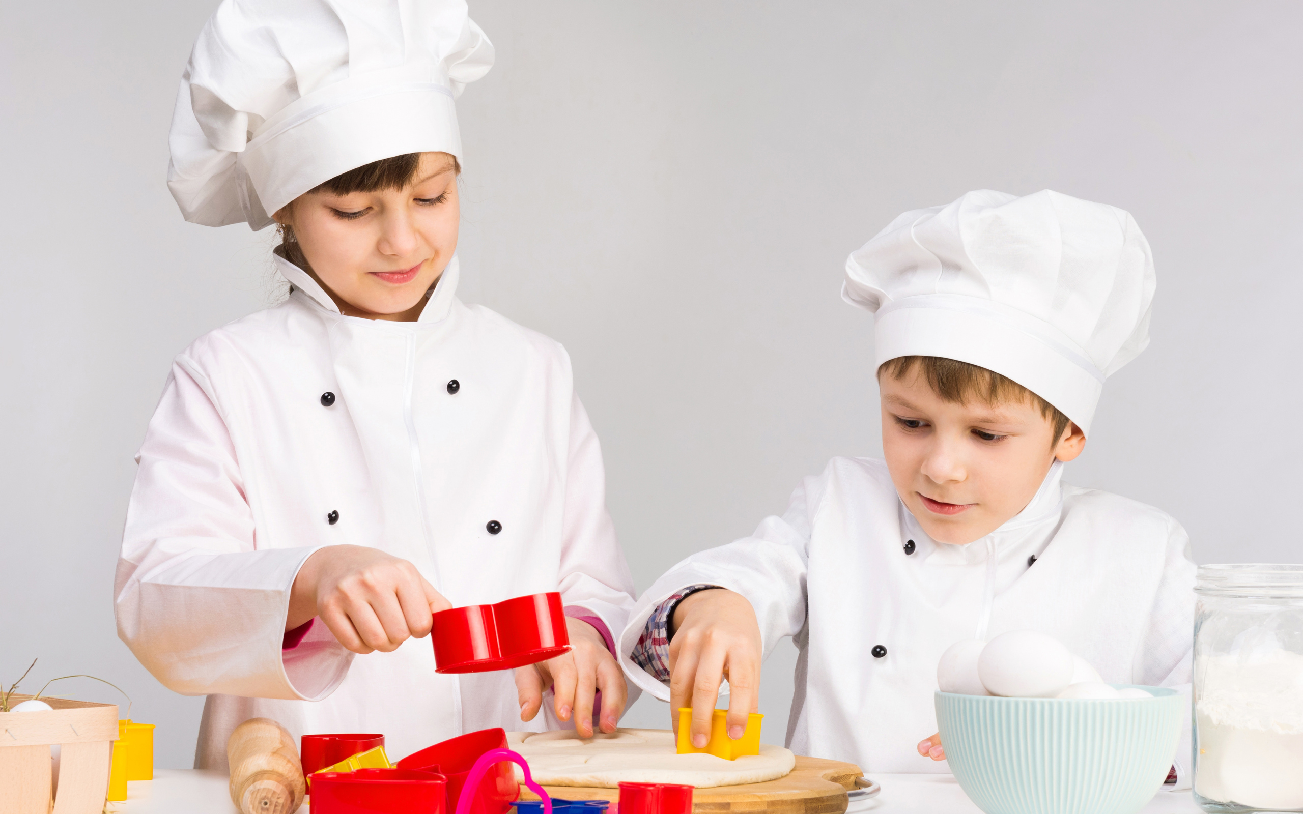 Маленькие мальчик и девочка готовят на кухне печенье