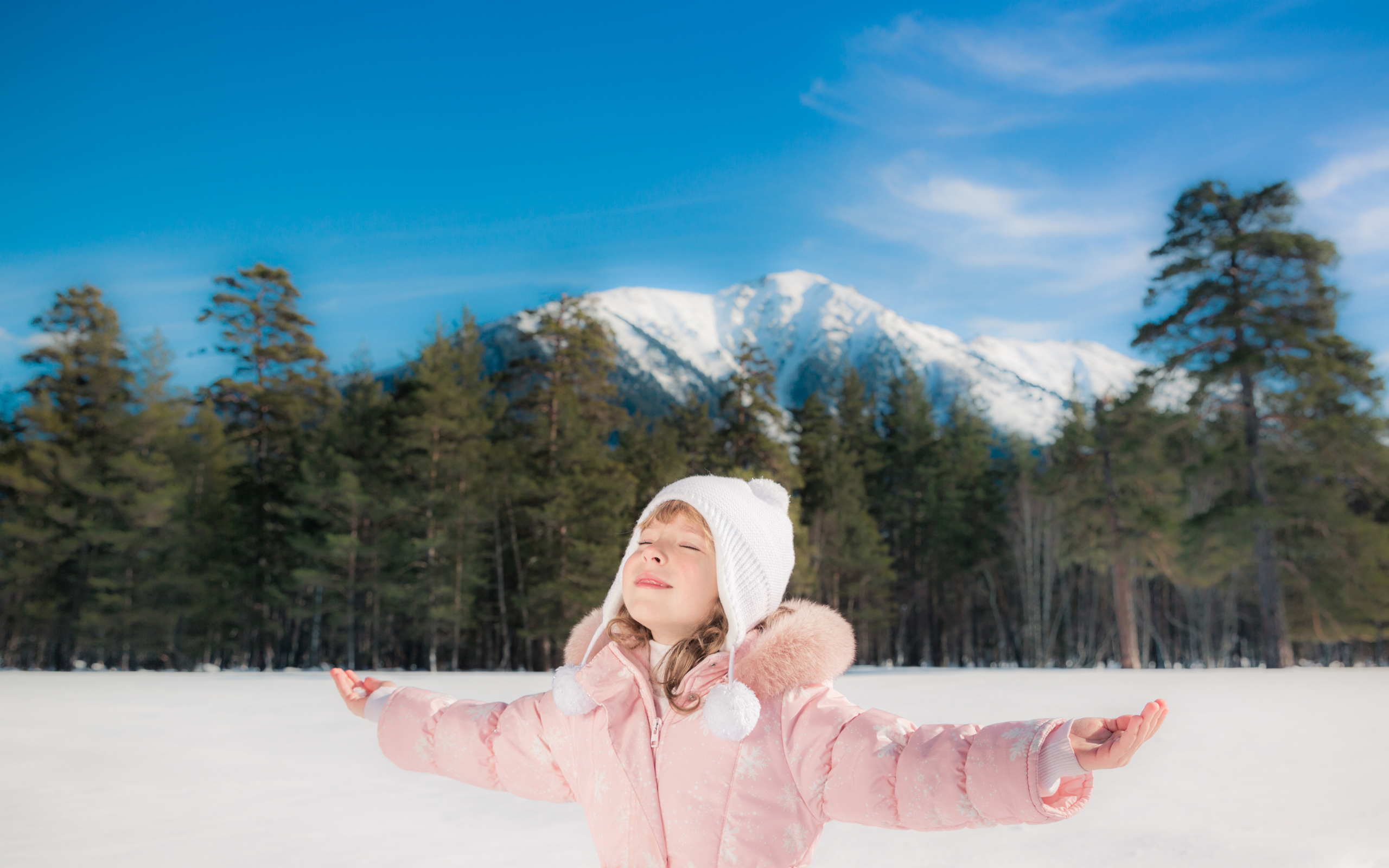 Маленькая девочка в розовой куртке на фоне гор зимой