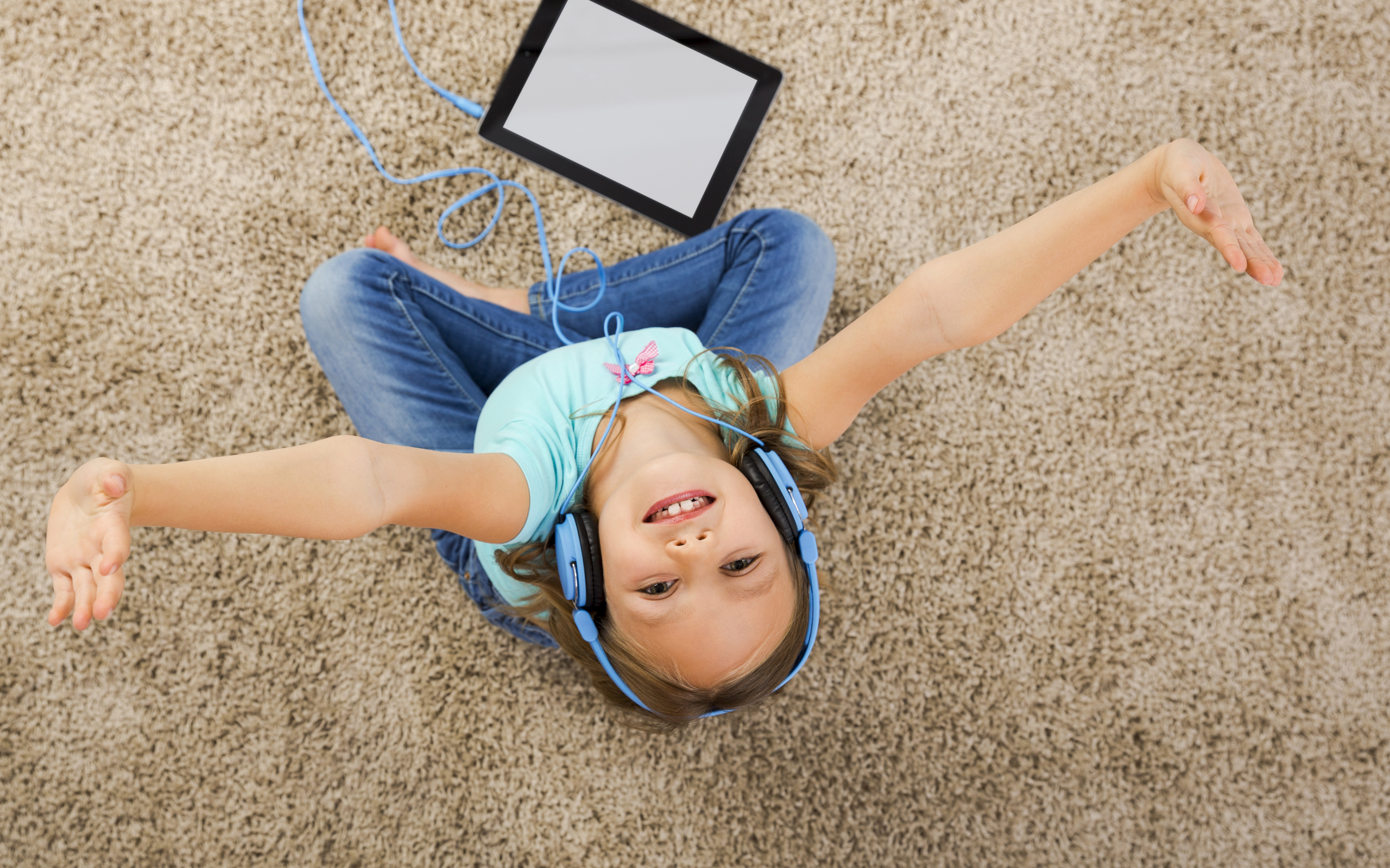 Маленькая девочка слушает музыку в наушниках сидя на ковре