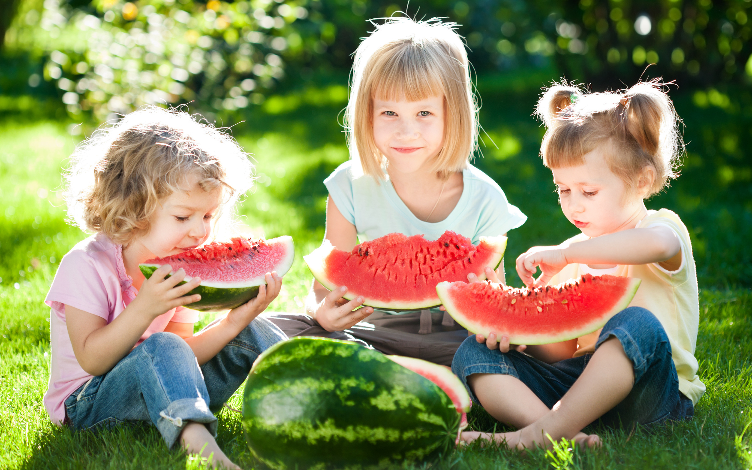 Три маленькие девочки едят арбуз на зеленой траве летом