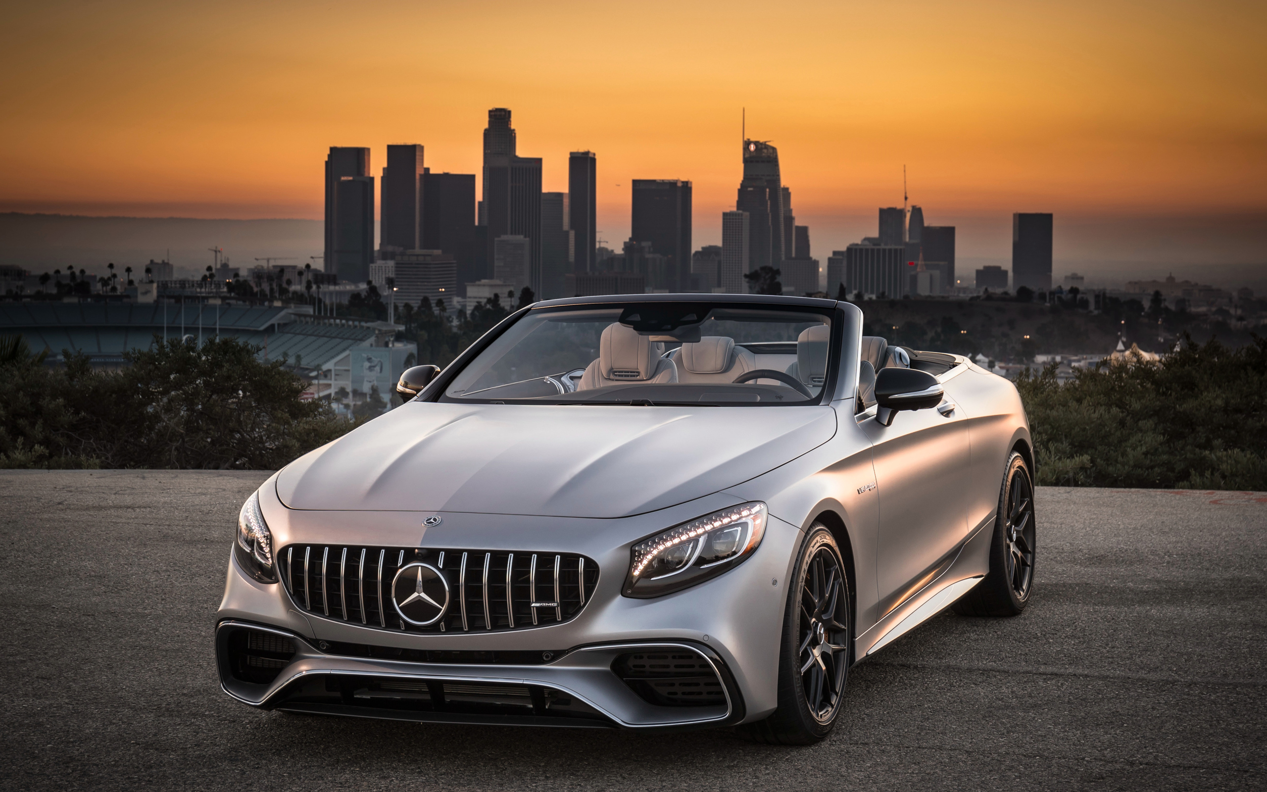 Серебристый автомобиль Mercedes AMG S63 4MATIC Cabriolet, 2018 на фоне мегаполиса
