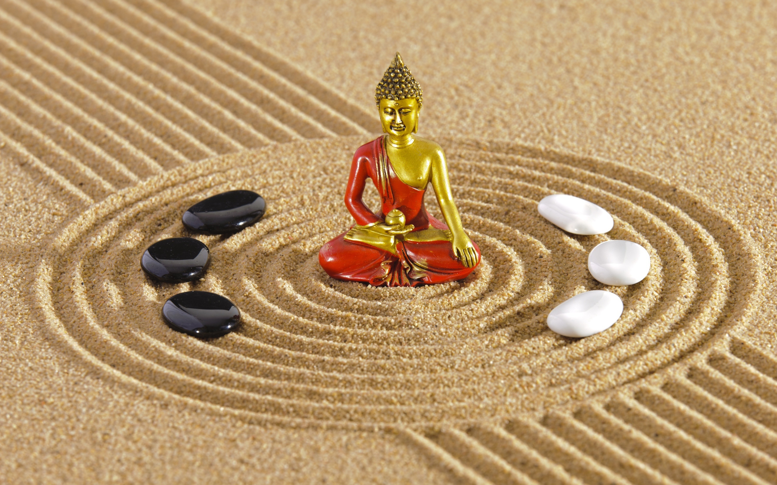 Статуэтка Будды стоит на песке с рисунком и камнями