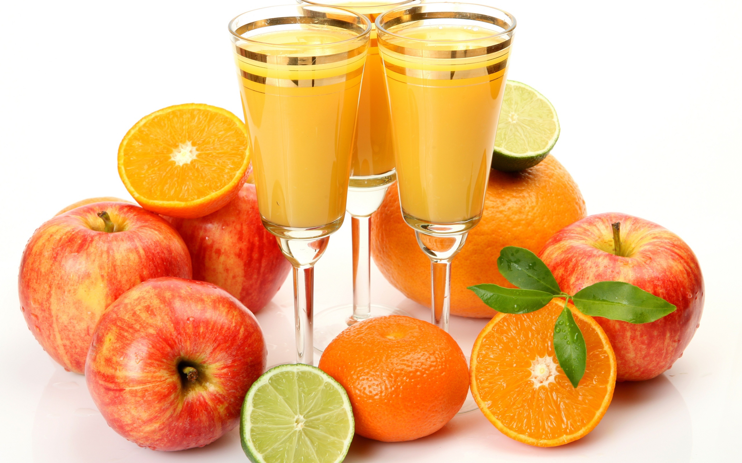 Три бокала сока на столе с яблоками и апельсинами на белом фоне