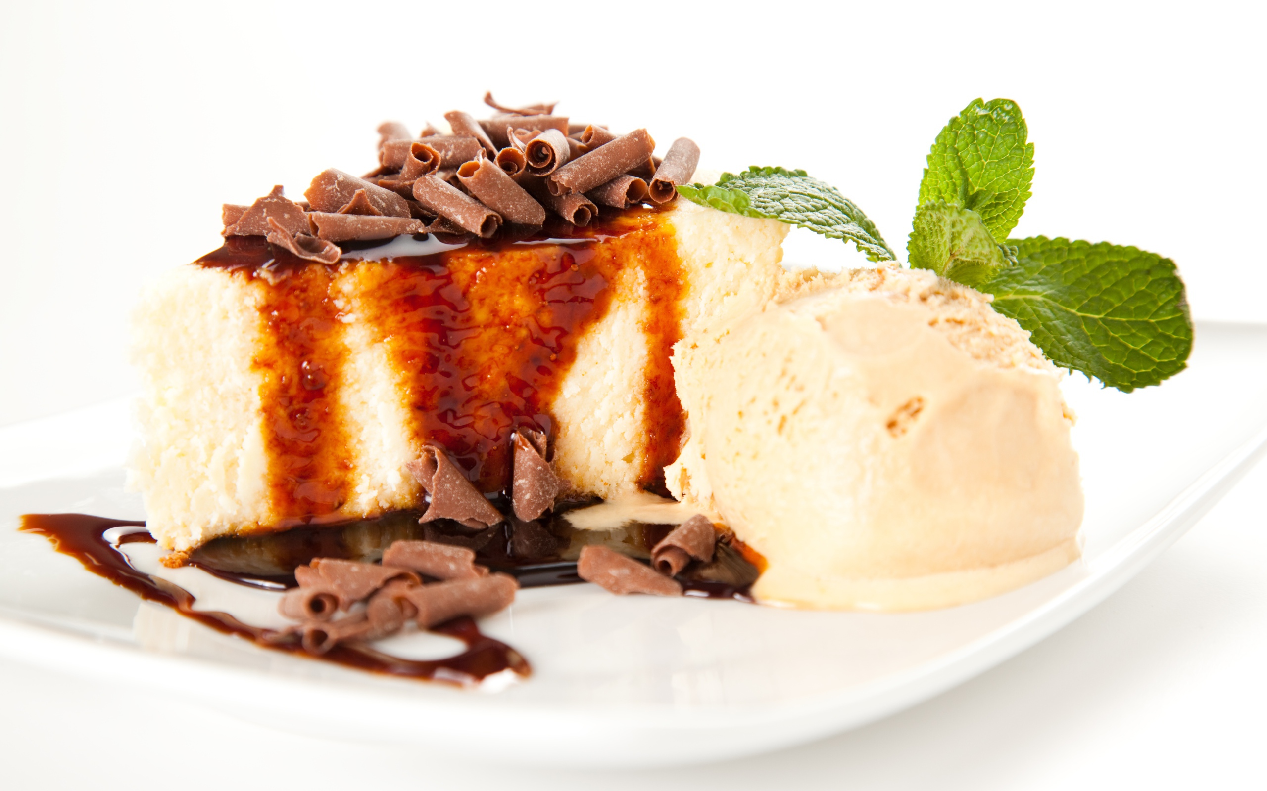 Кусок чизкейка с шоколадом и шариком мороженого на белой тарелке 