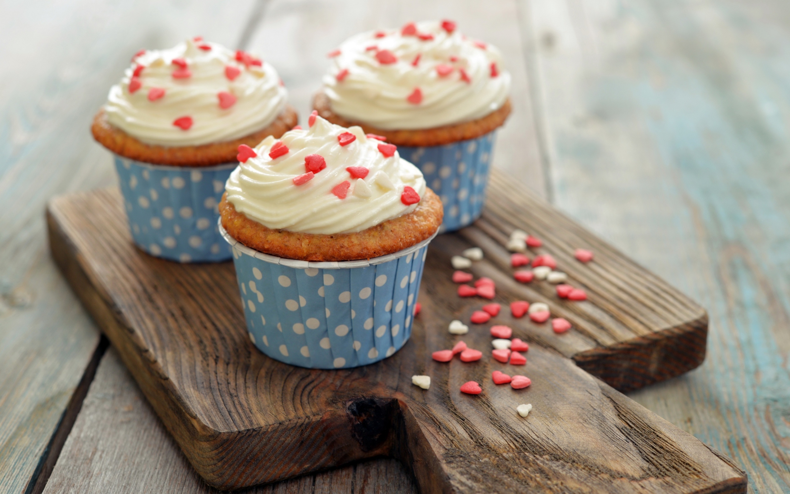 Три кекса со сливками украшены сердечками стоят на разделочной доске