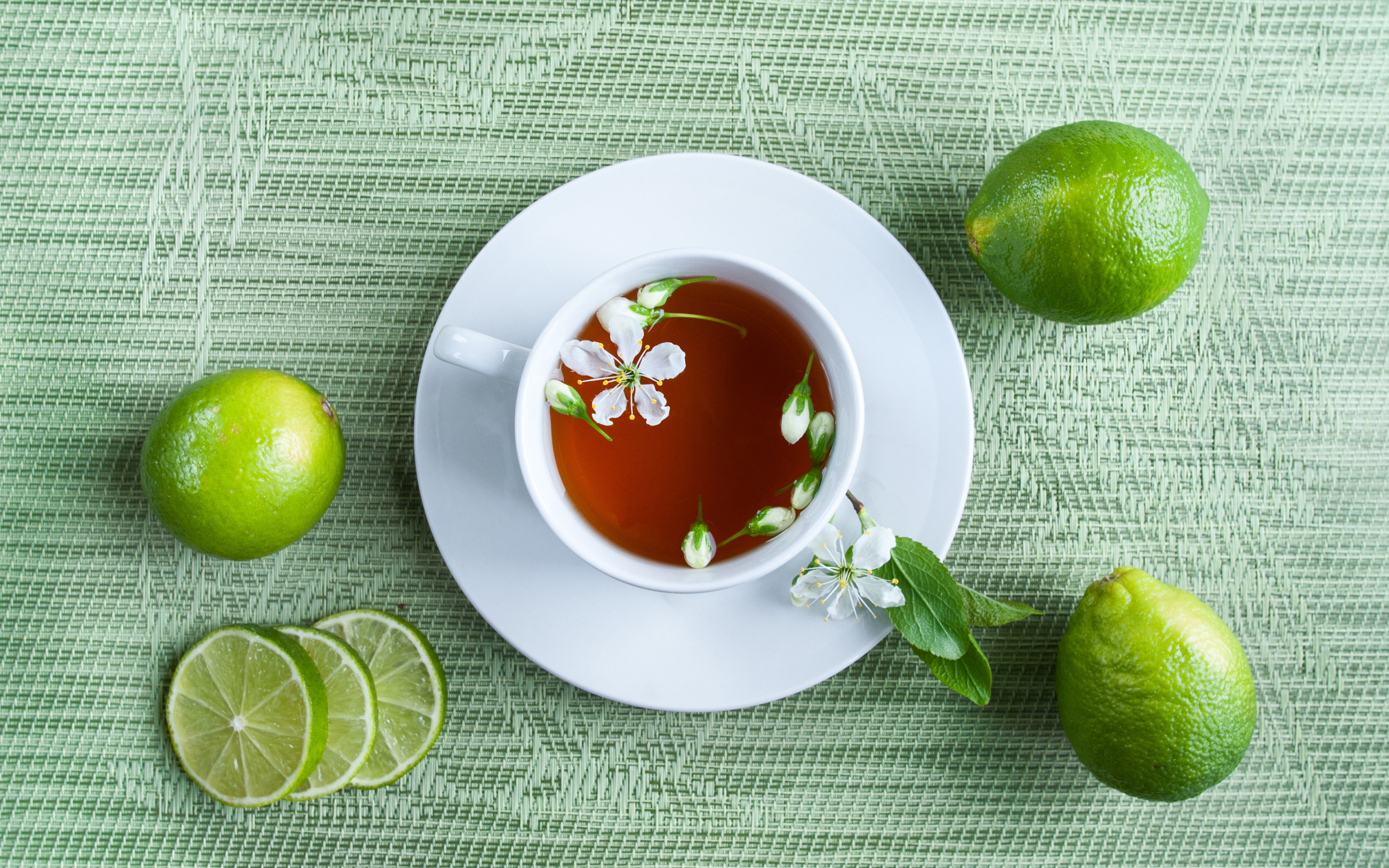 A cup of tea with green limes on the table
