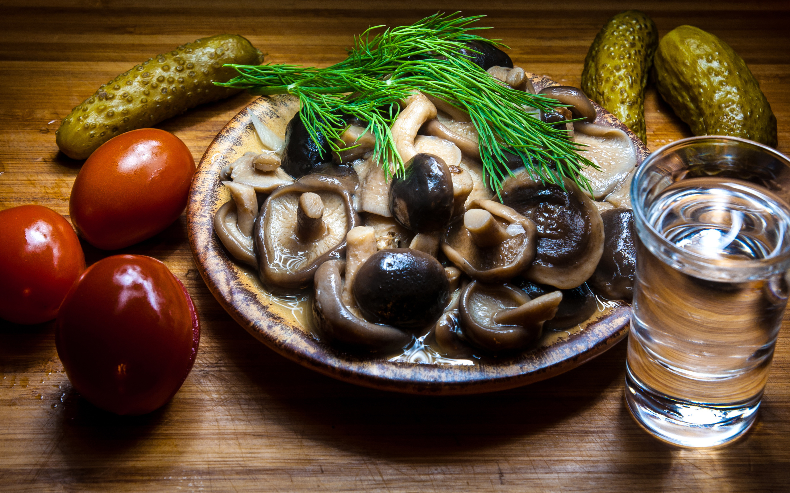 Рюмка водки на столе с солеными грибами, помидорами и огурцами